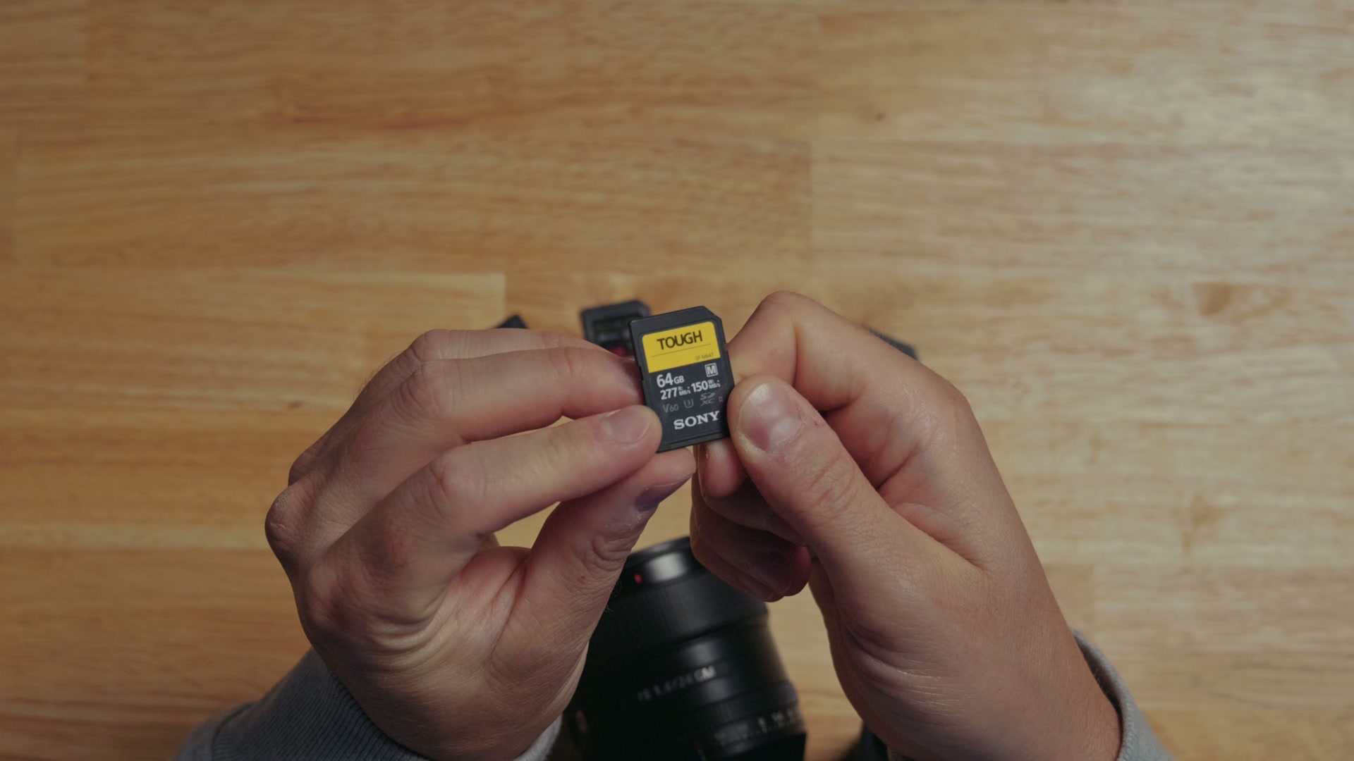 A Sony TOUGH 64GB SD card held between two hands, with the V60 speed rating printed on the front sticker