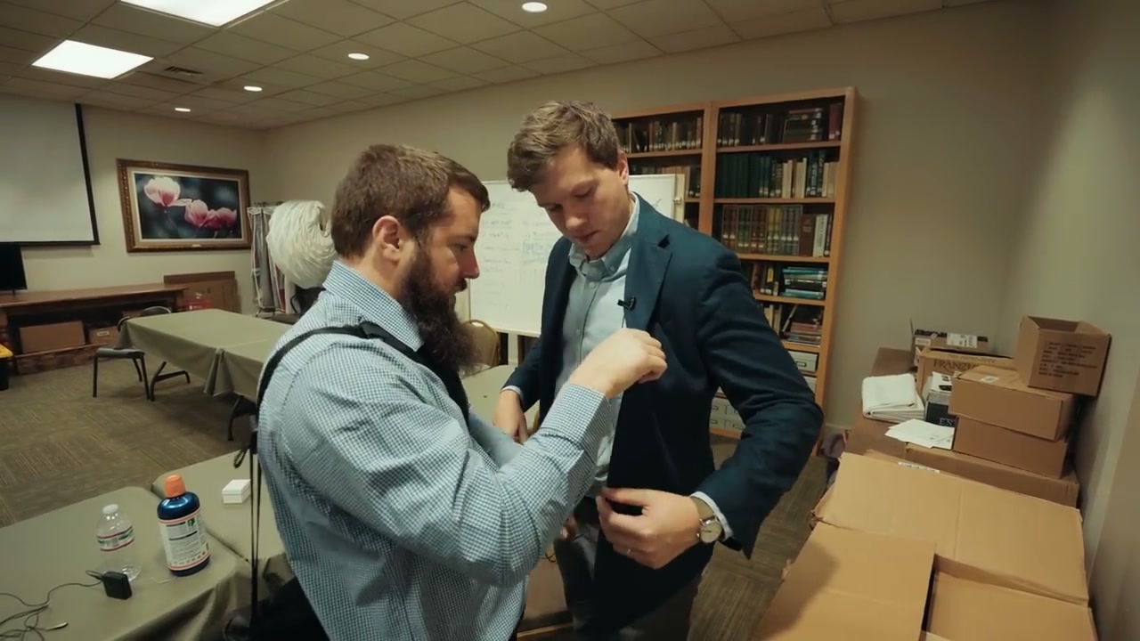 A lavalier microphone being clipped to the lapel of a groom's suit jacket