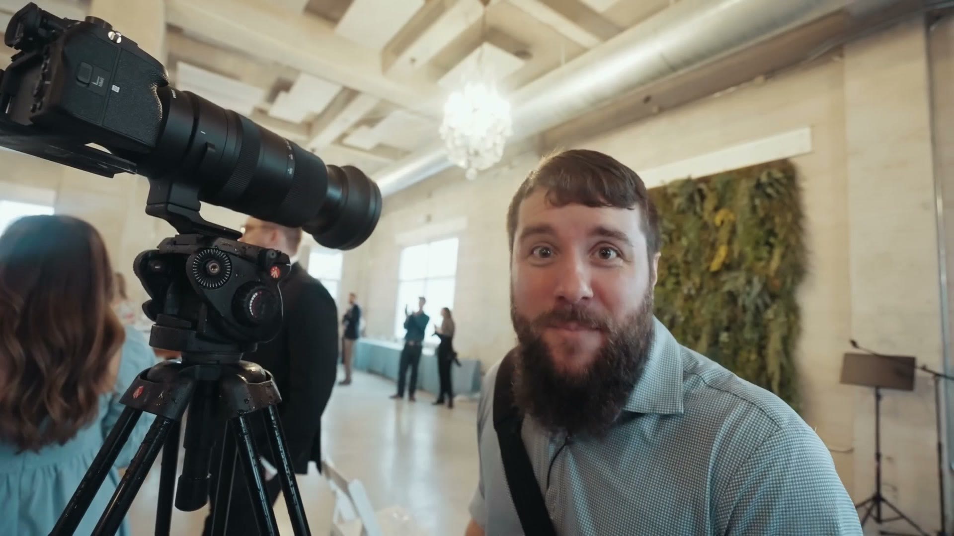 A camera with a large telephoto lens on a tripod at the back of a ceremony space
