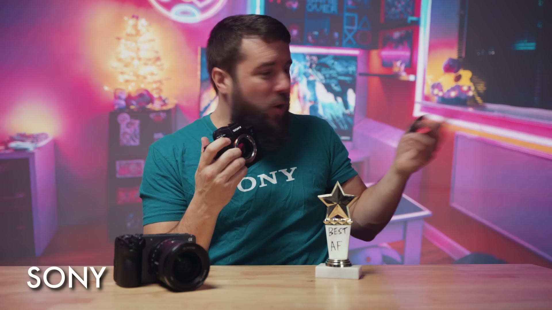 Matt dressed as Sony in a teal Sony t-shirt, holding a camera body, with a trophy on the desk reading Best AF