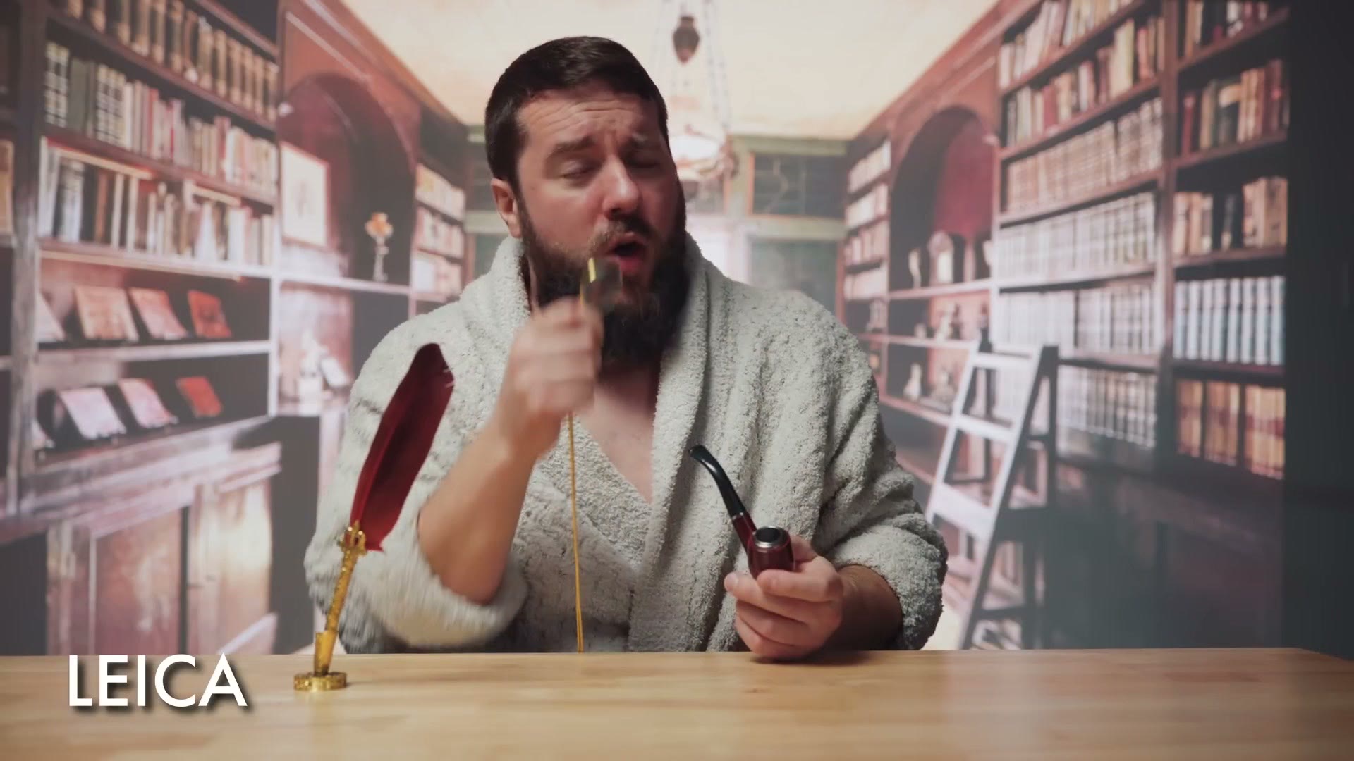 Matt dressed as Leica in a bathrobe in a library, holding a pipe next to a quill pen