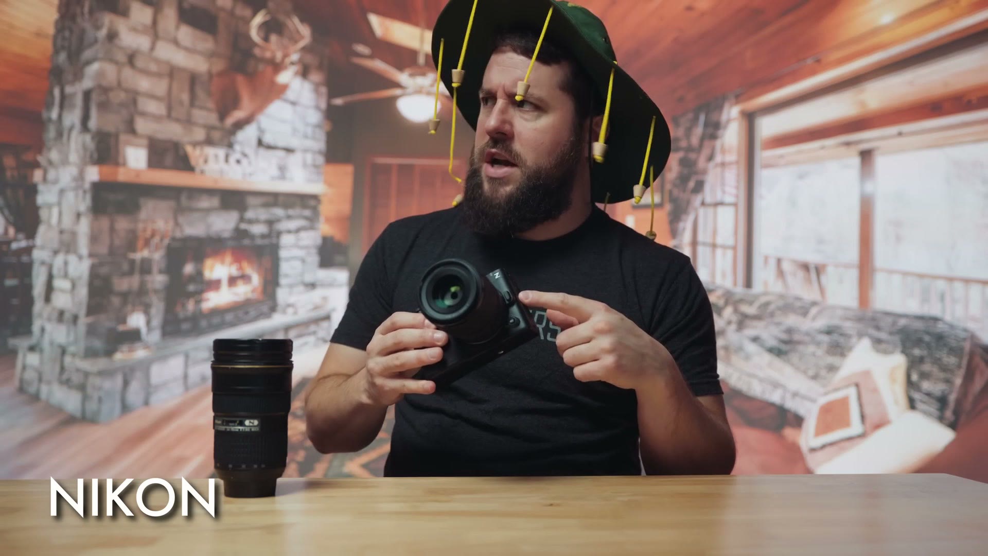 Matt dressed as Nikon in a hat hung with yellow tassels, holding a camera in a wood cabin
