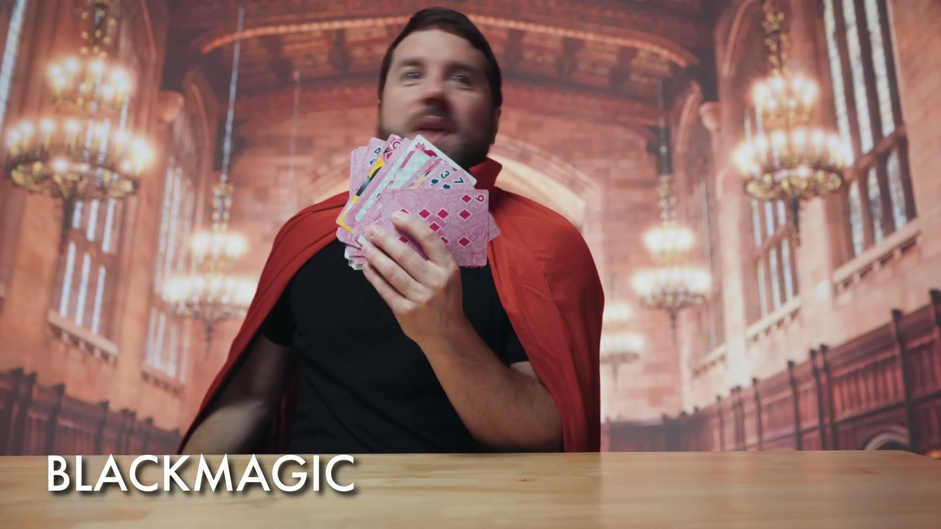 Matt dressed as Blackmagic in a red cape, fanning out a deck of playing cards in a grand hall