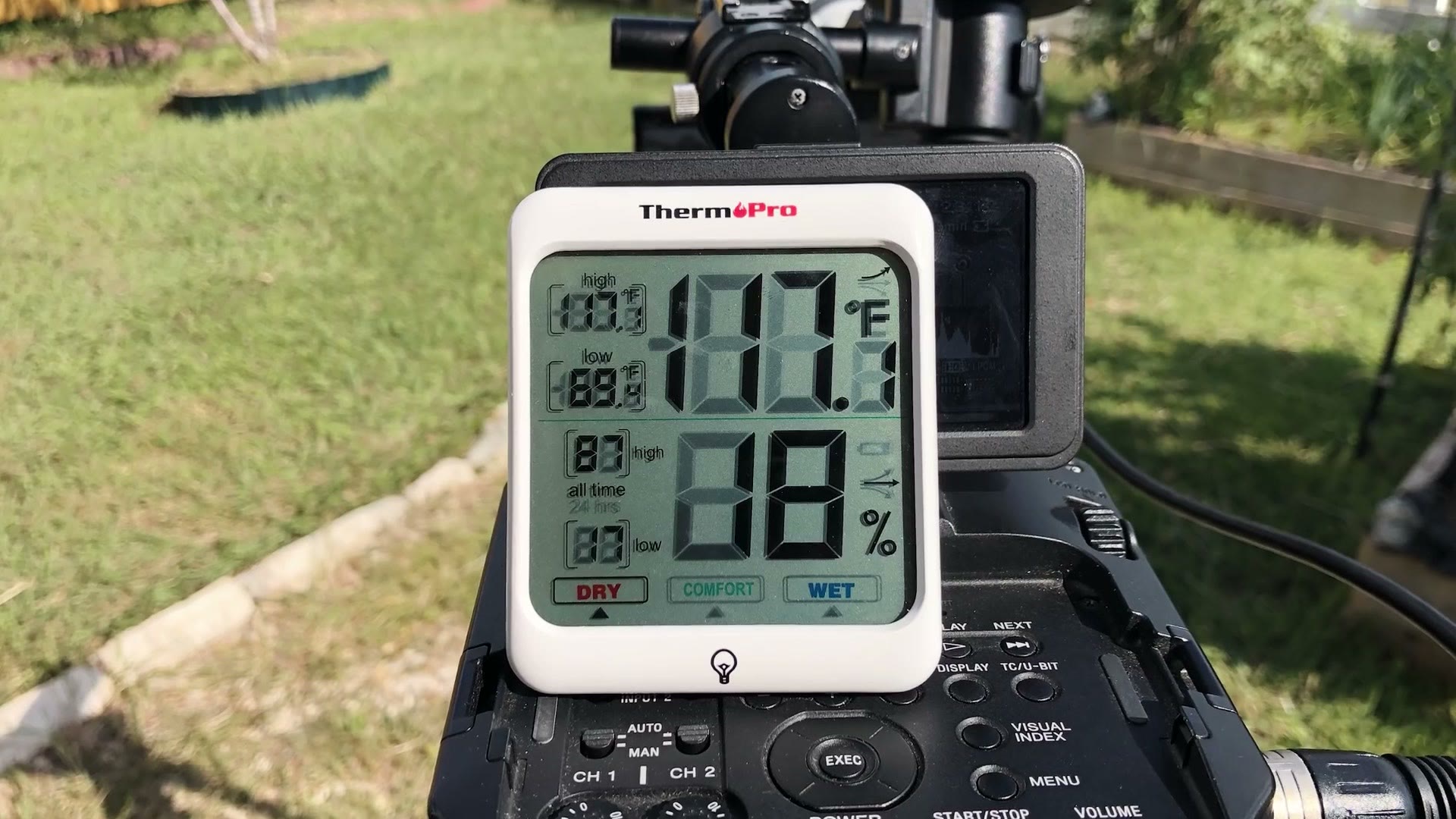A ThermoPro temperature and humidity meter sitting beside the camera outdoors reading 117 degrees Fahrenheit