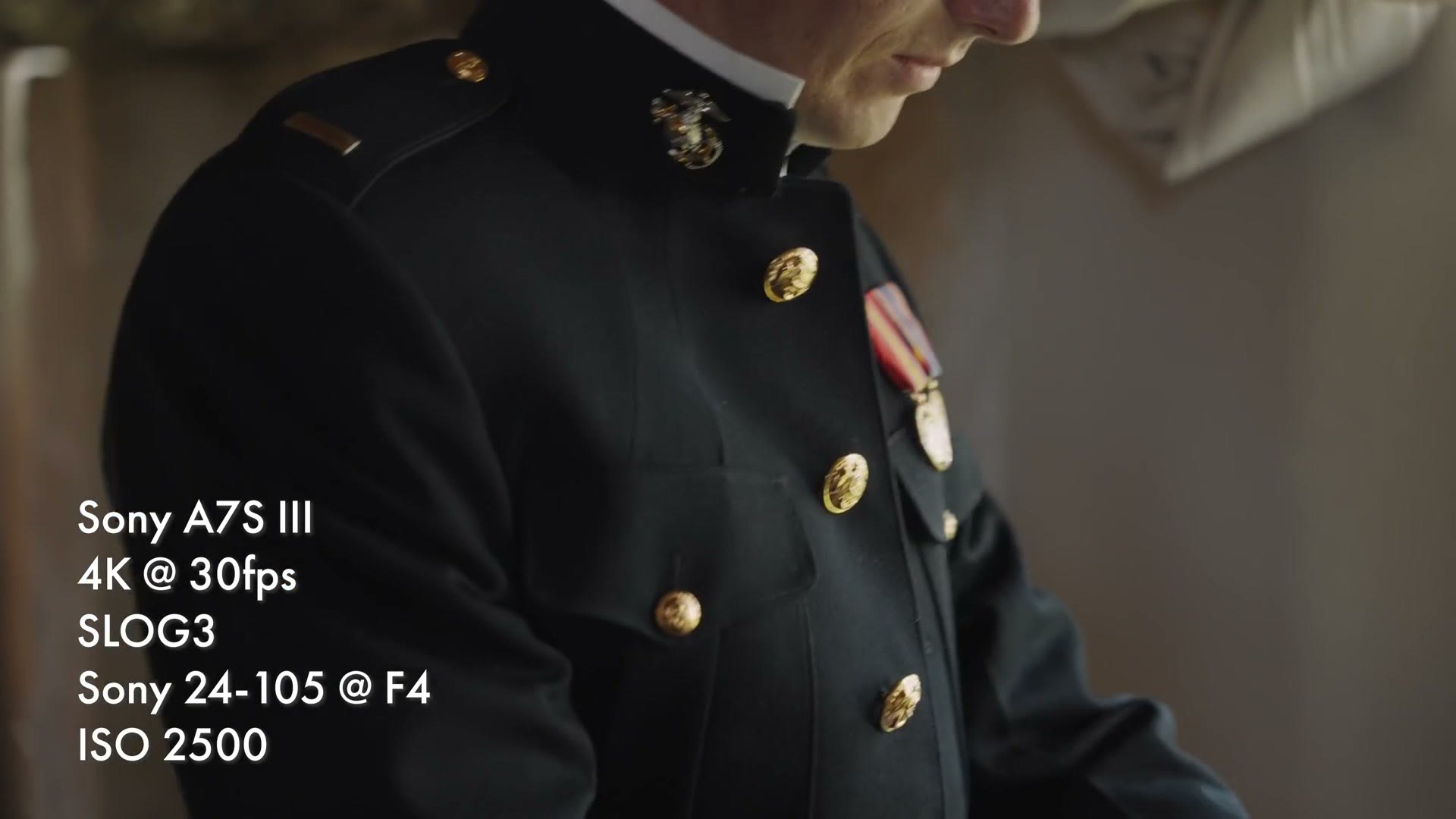 A close detail of a dark Marine dress uniform jacket with gold buttons and medals, lit by window light indoors, overlay reading 4K at 30fps, SLOG3, ISO 2500