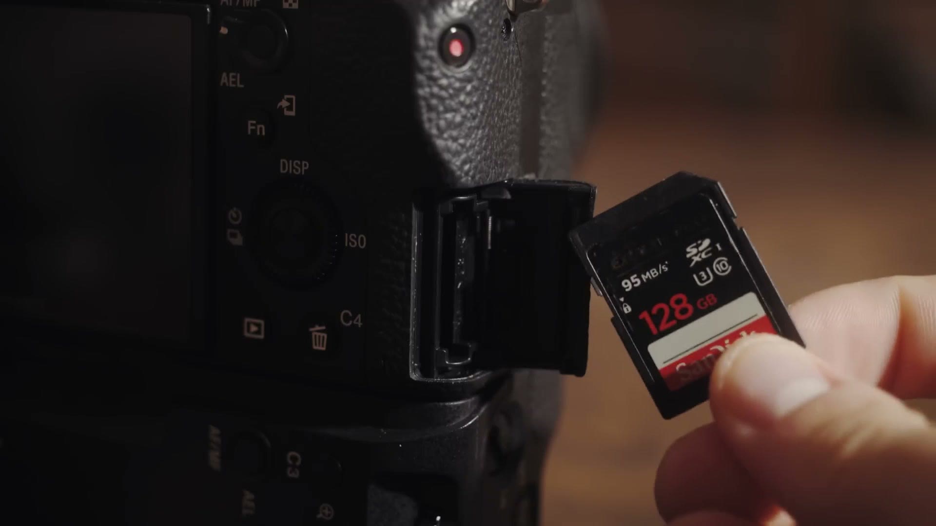 A hand sliding a SanDisk Extreme Pro 128GB SD card into the open card door of a Sony mirrorless camera