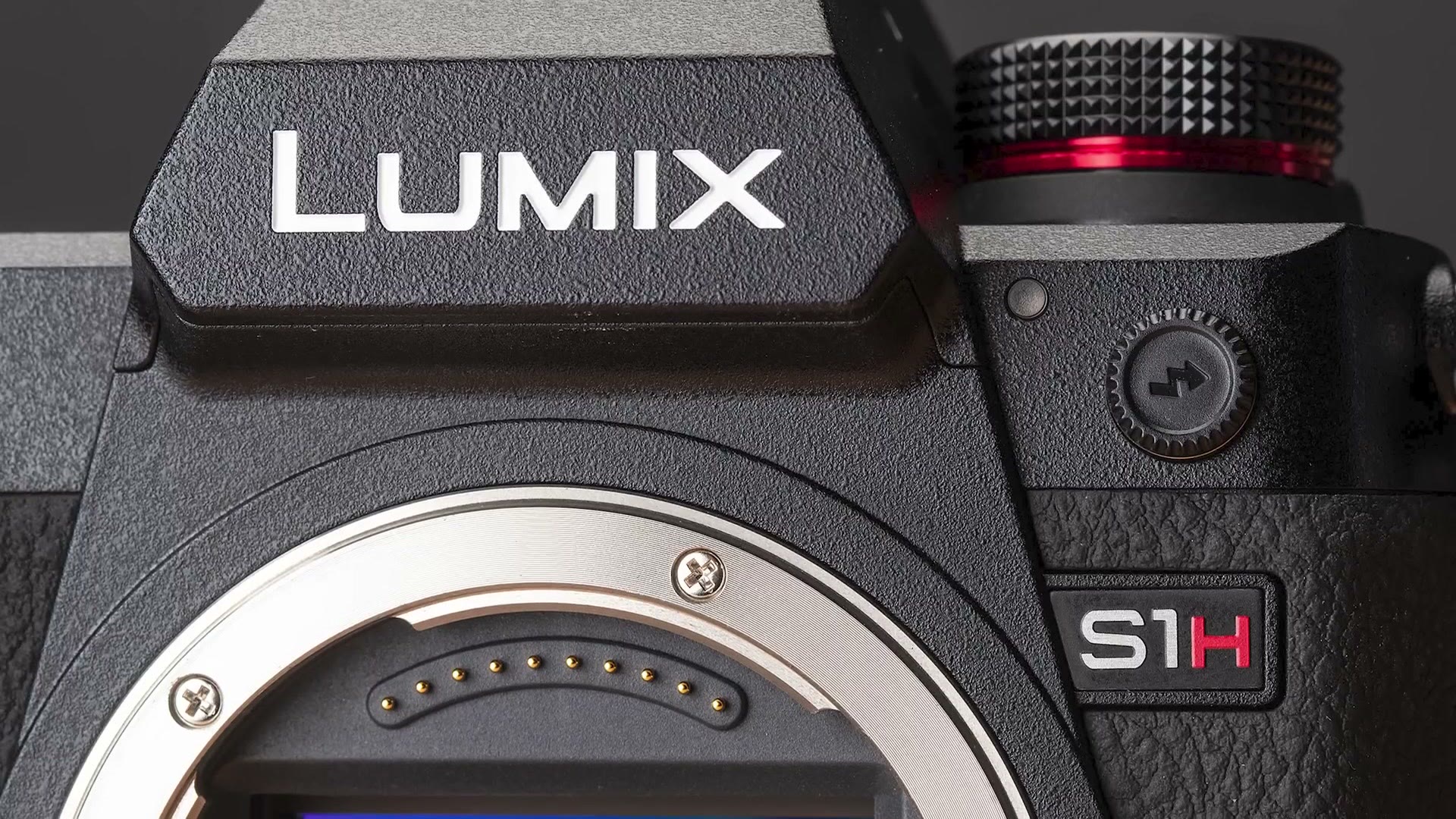 A close up of the front of a Panasonic Lumix S1H body showing the LUMIX and S1H badges and the open lens mount