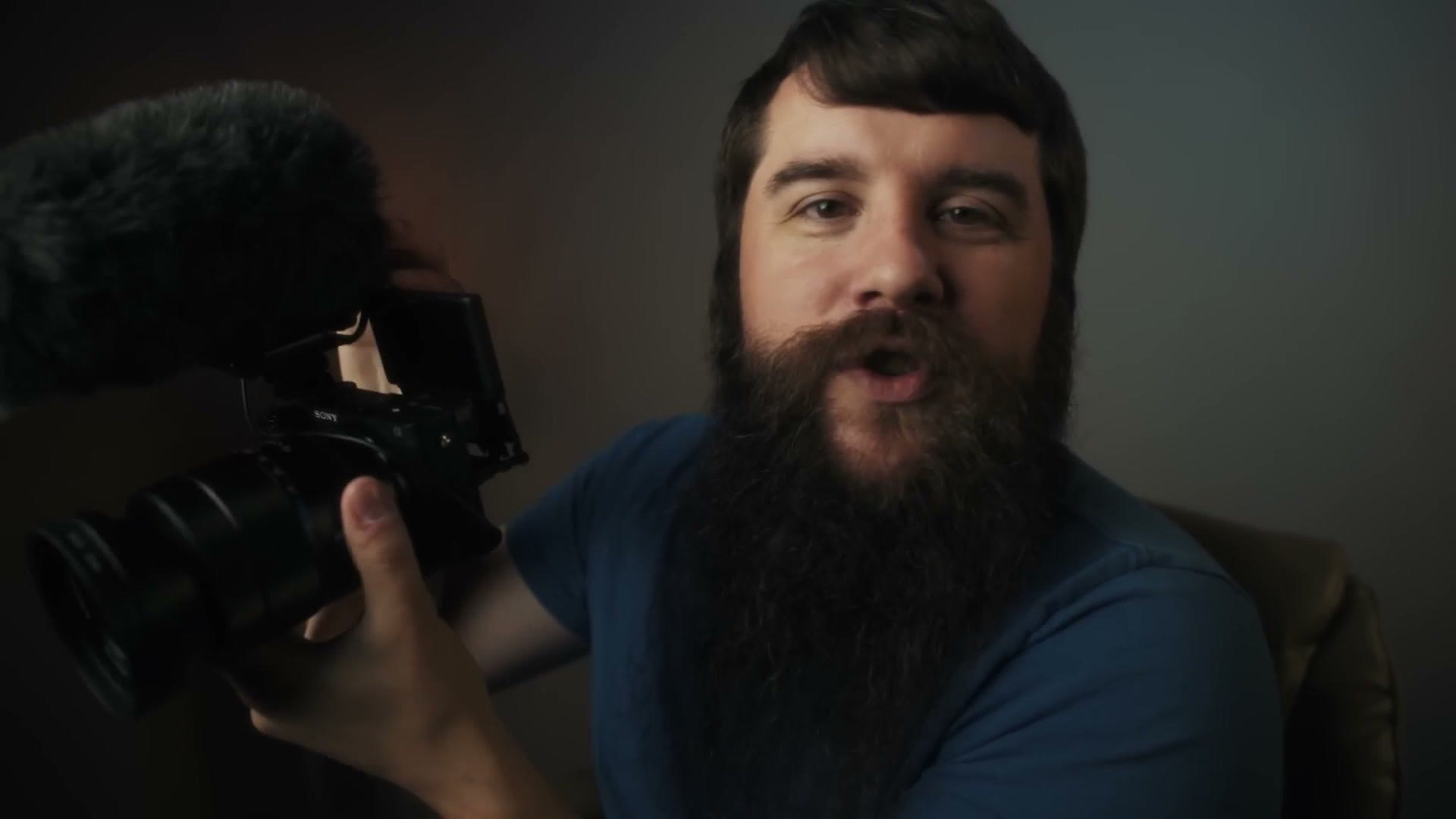 Matt holding up a Sony mirrorless camera with a microphone on top and the rear screen tilted up toward him