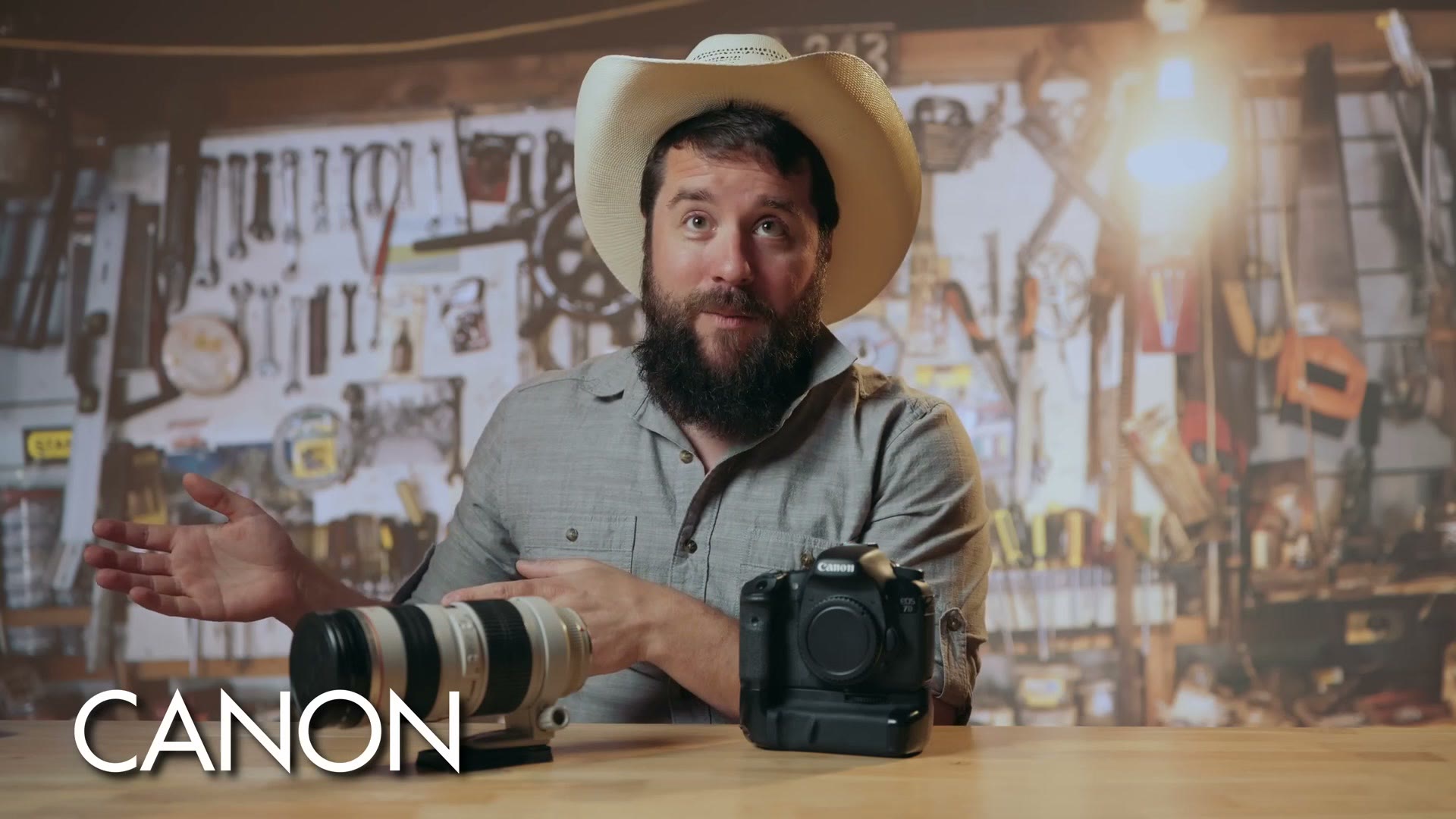 Matt in a straw cowboy hat in a workshop with a Canon body and a white telephoto lens on the table, captioned CANON