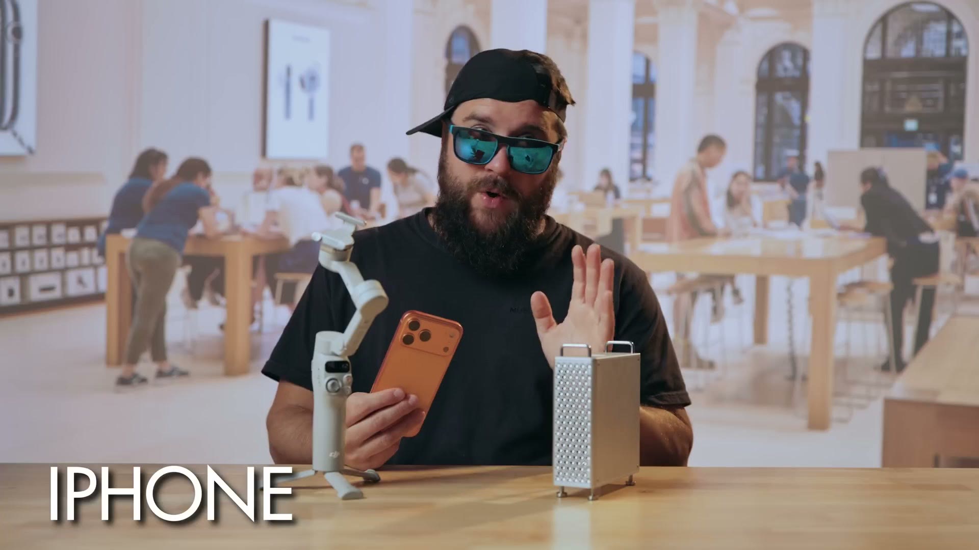 Matt in sunglasses and a backwards cap inside an Apple Store, holding a phone on a gimbal beside a Mac Pro, captioned IPHONE