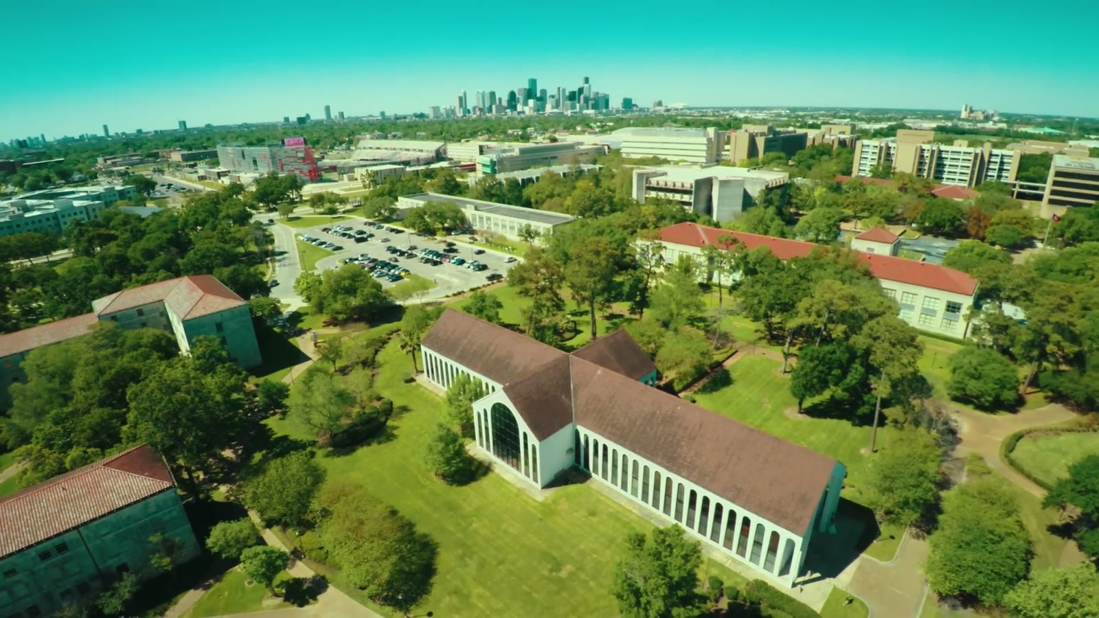 Aerial drone view of a colonnaded chapel on a green campus with the Houston skyline in the distance
