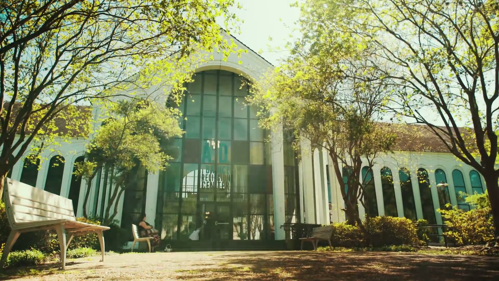 Exterior of the glass-fronted chapel entrance framed by arched colonnades and trees, a guest seated on a bench