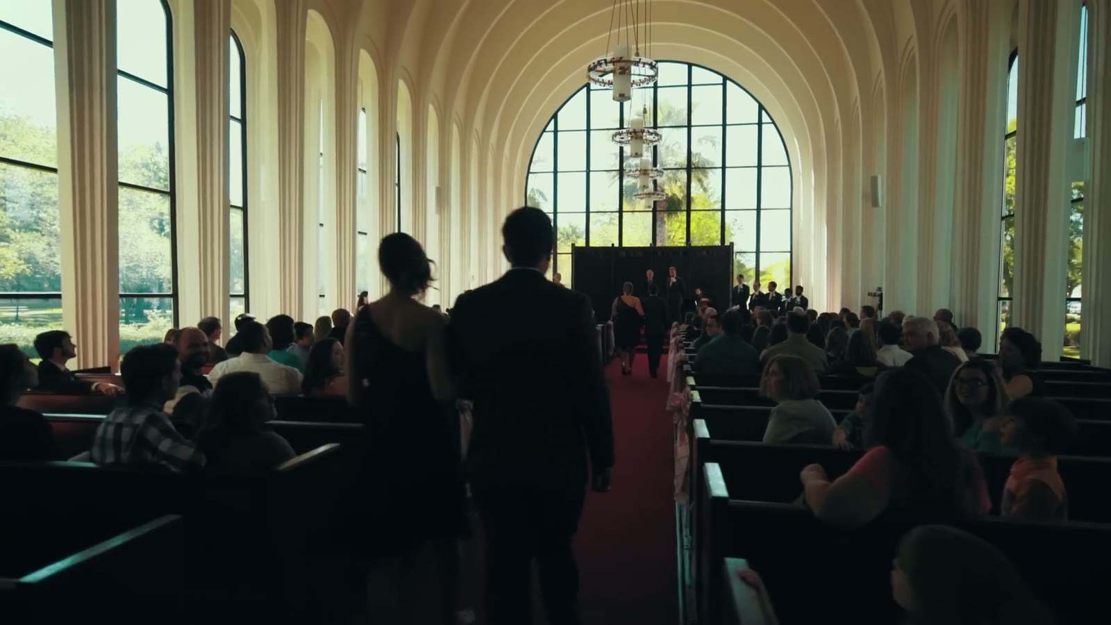 View down the chapel aisle from the back pews toward the altar during the ceremony, red carpet underfoot
