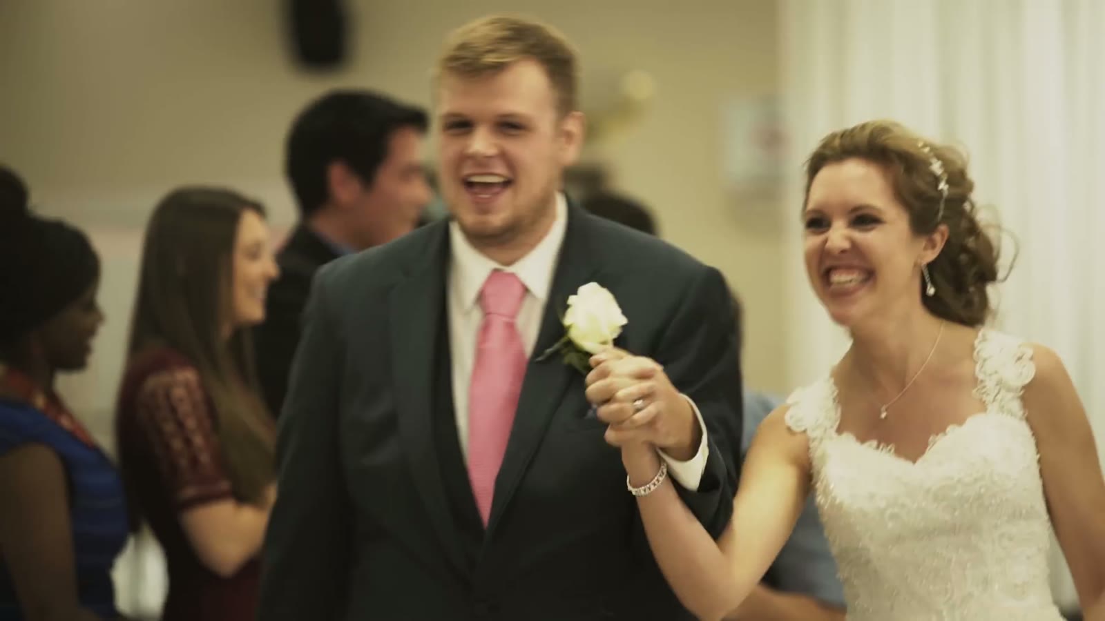 Newlyweds laughing and holding hands walking through the reception as guests look on behind them