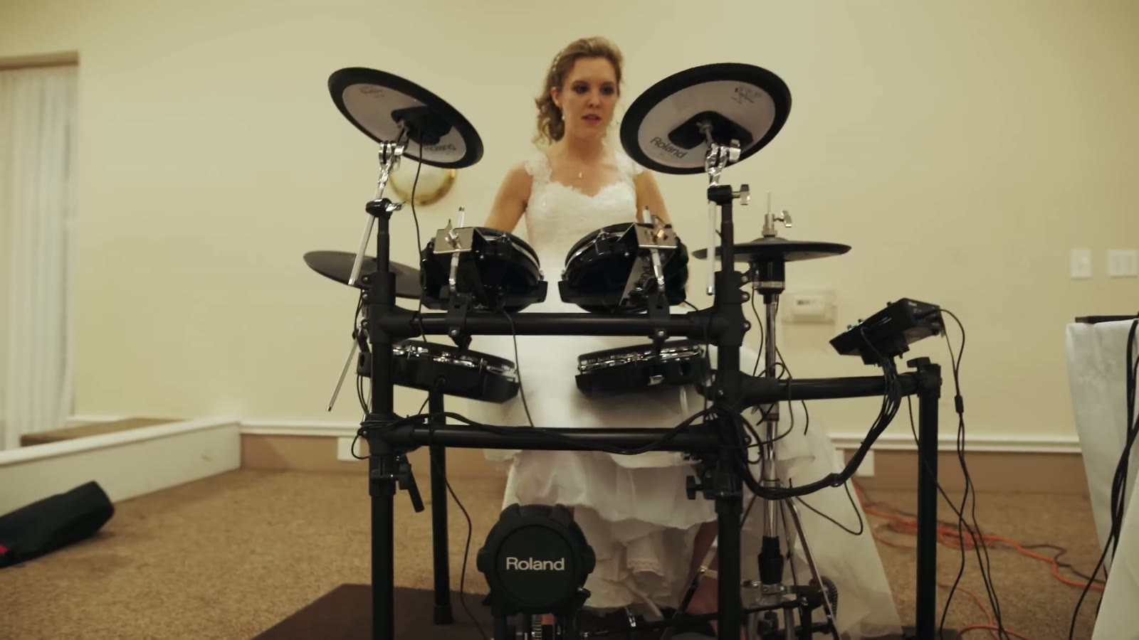 Bride in her wedding dress playing an electronic Roland drum kit set up in the reception hall
