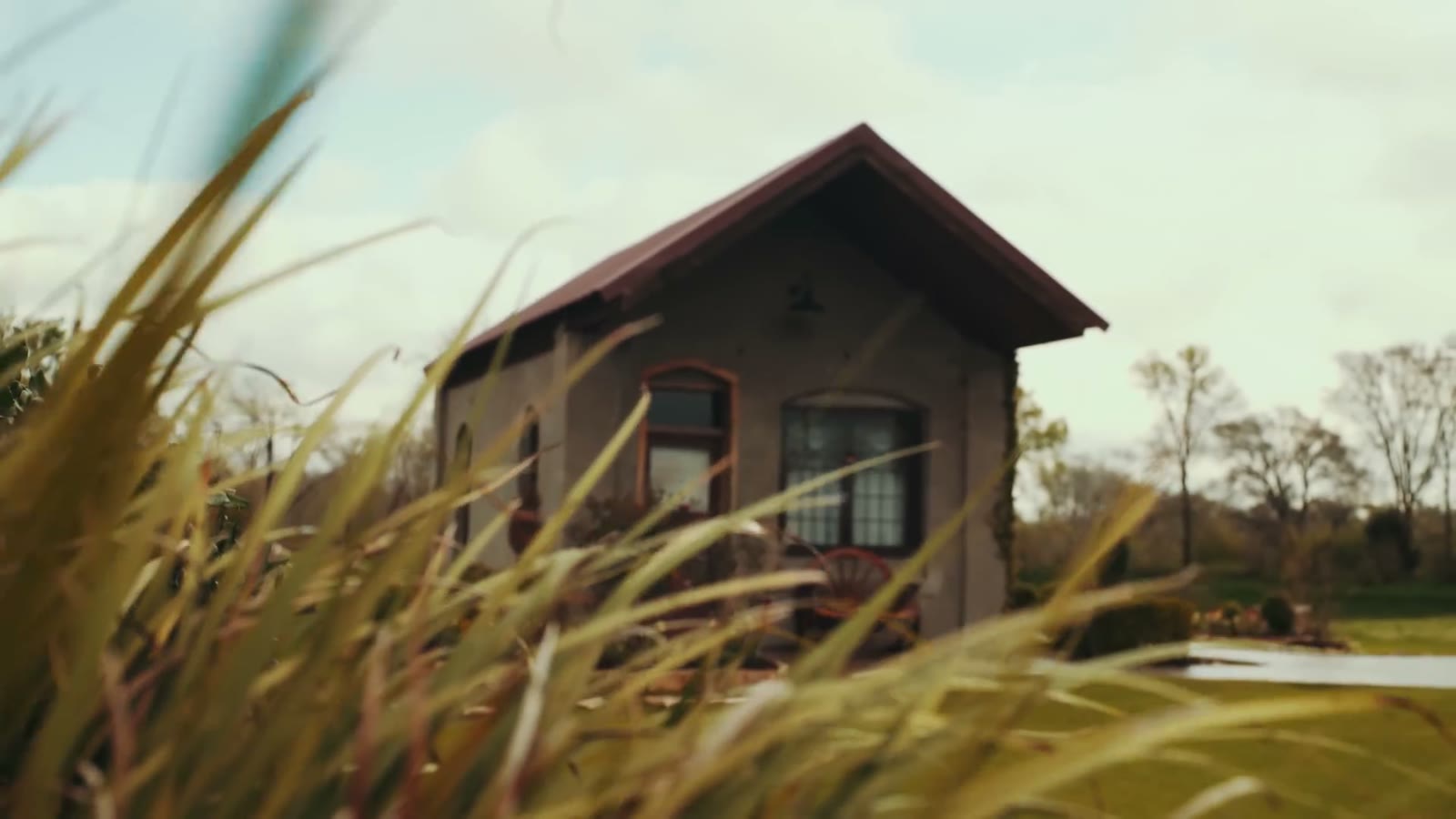 Rustic countryside venue building with a red metal roof and covered porch, shot through tall grass