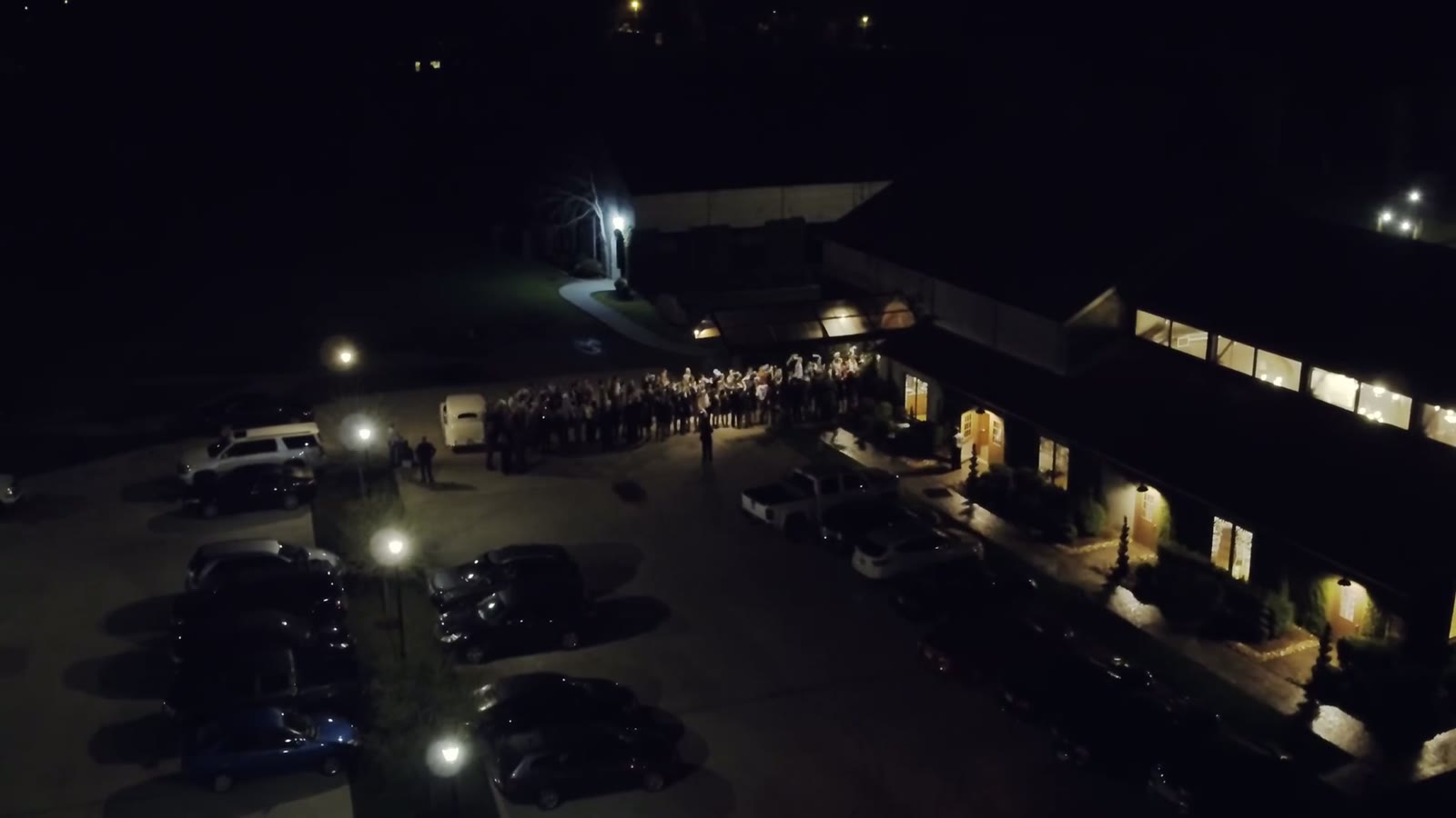 Aerial night shot of guests gathered outside the venue entrance among parked cars
