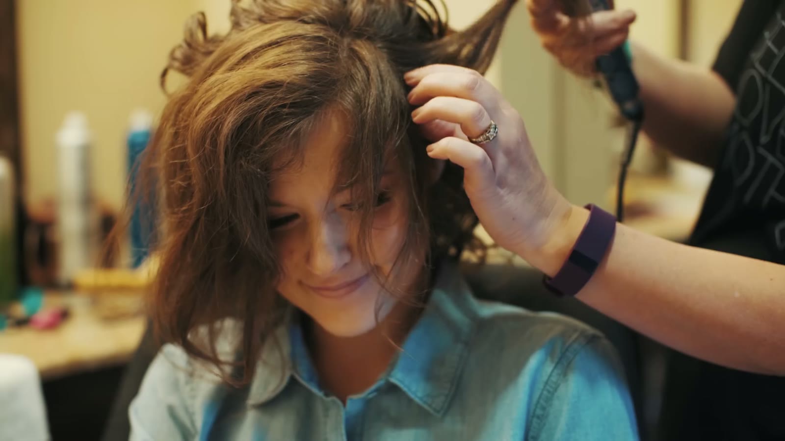 Bride getting her hair curled with a curling iron, stylist's hand holding sections up near her scalp