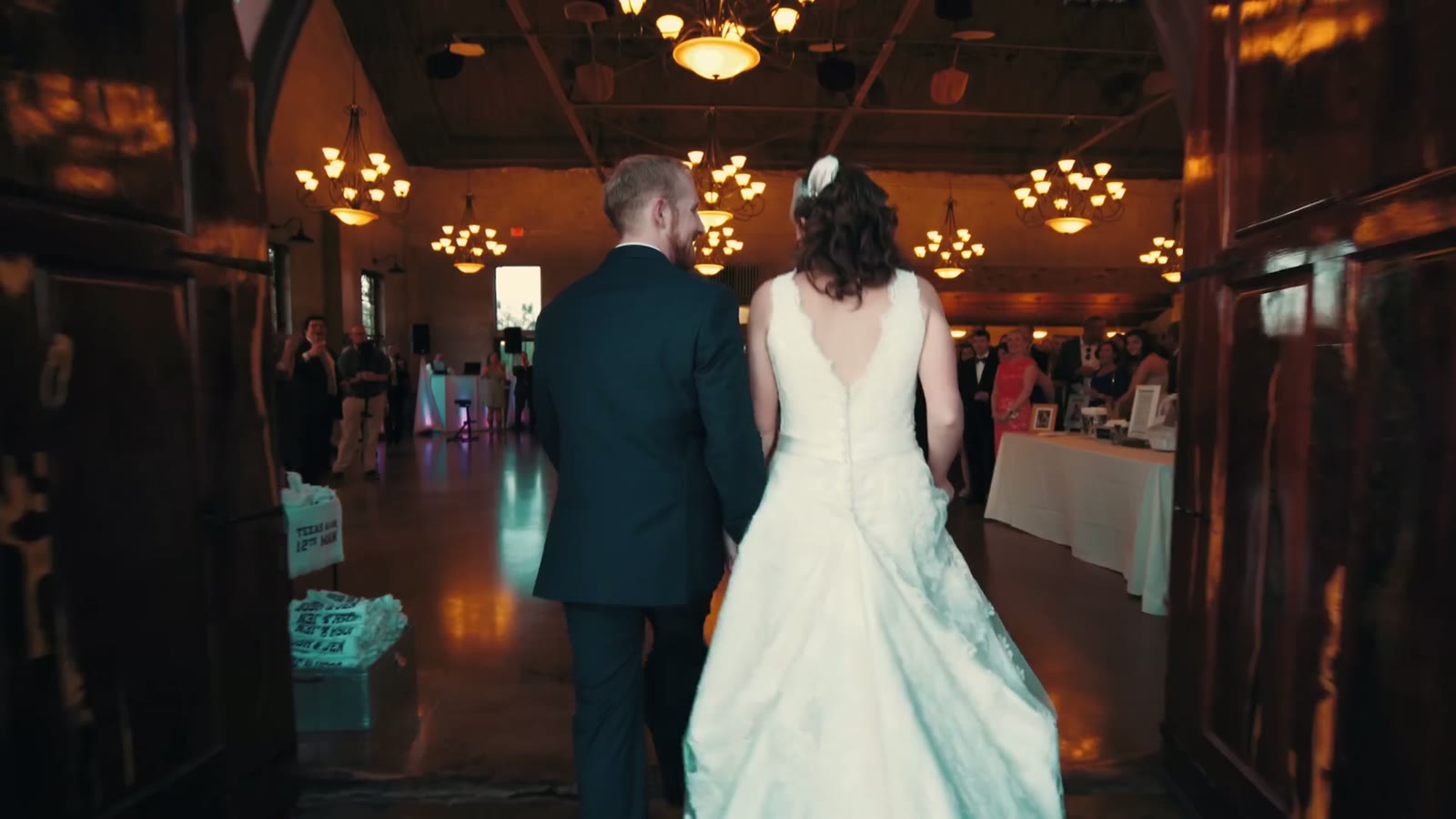 Bride and groom seen from behind walking into the reception hall under rows of chandeliers