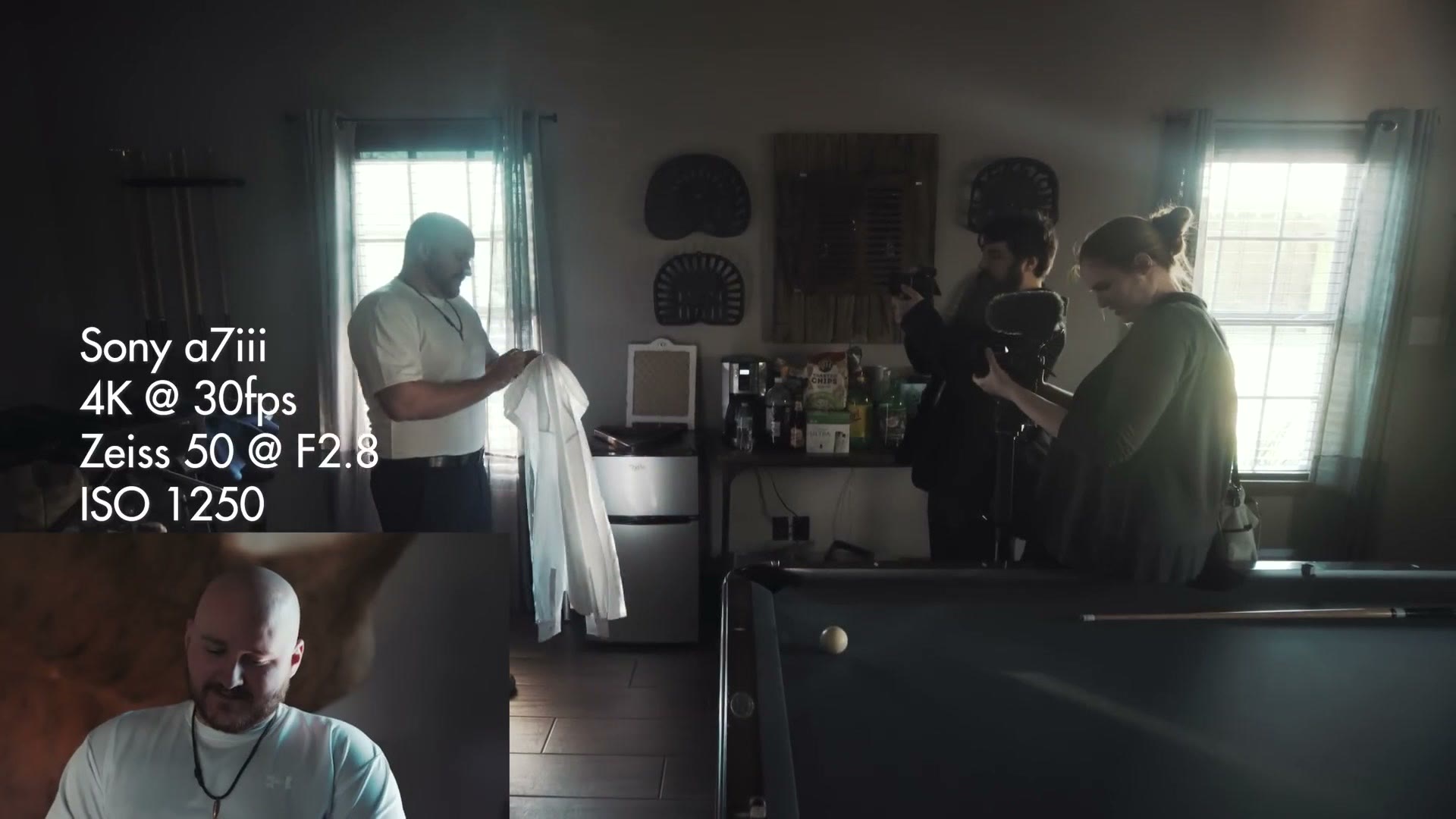 A groom standing on a marked spot beside a window buttoning his shirt while two shooters film him, with on-screen text reading Sony a7iii, 4K at 30fps, Zeiss 50 at F2.8, ISO 1250 and an inset of the resulting shot.