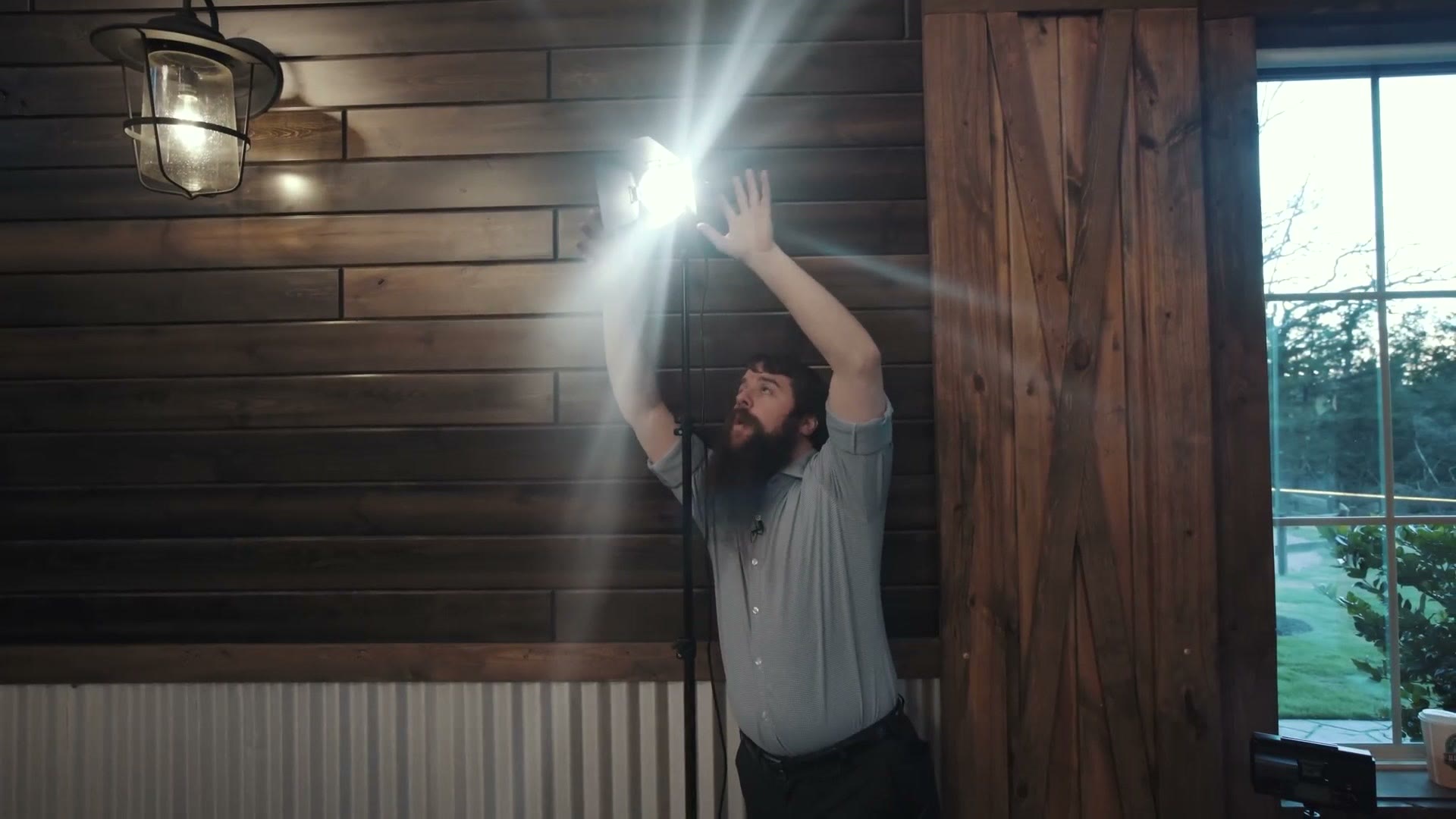 Matt reaching up to adjust a lit Practilite spotlight on a stand inside a barn reception space, its beam throwing across the timber wall.