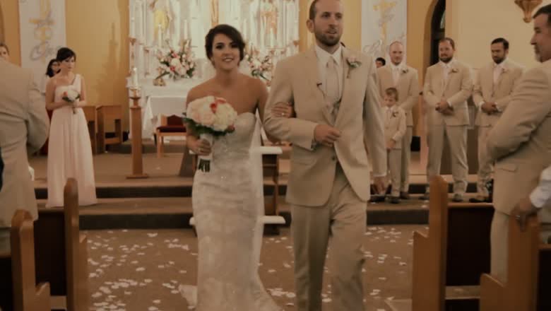 The bride and groom walking back down the church aisle through scattered petals, the wedding party still standing at the front