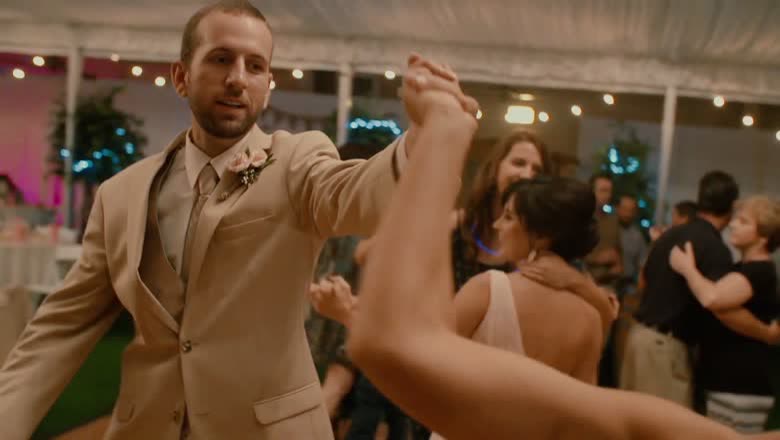 The groom spinning a dance partner under string lights in the reception tent, the floor full of people dancing