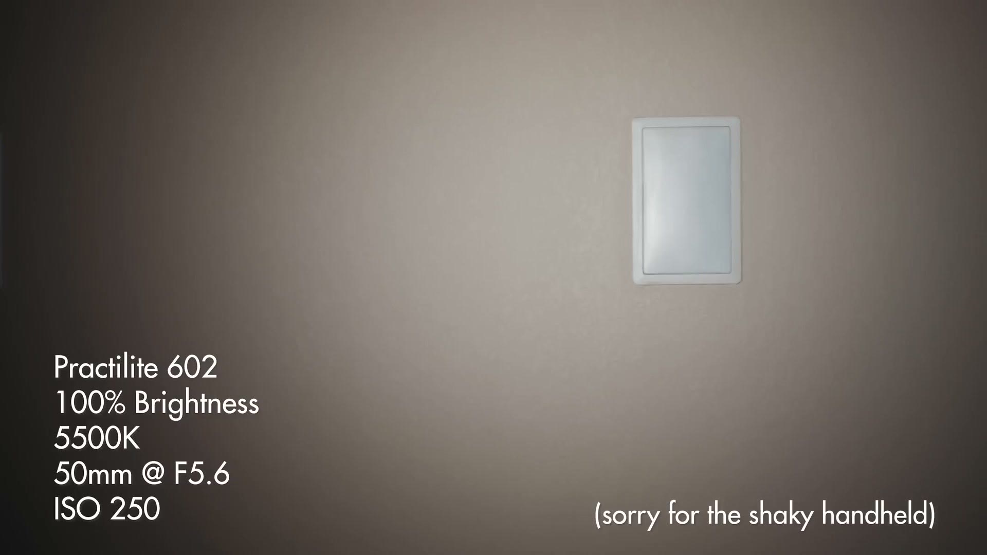 A wall lit by a spotlight with a light switch in frame, overlaid with the text Practilite 602, 100% brightness, 5500K, 50mm at F5.6, ISO 250.