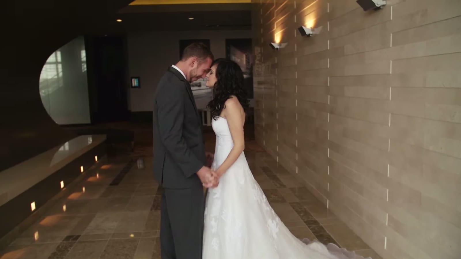 Bride and groom holding hands forehead to forehead in a dim hallway lit by string lights along the floor