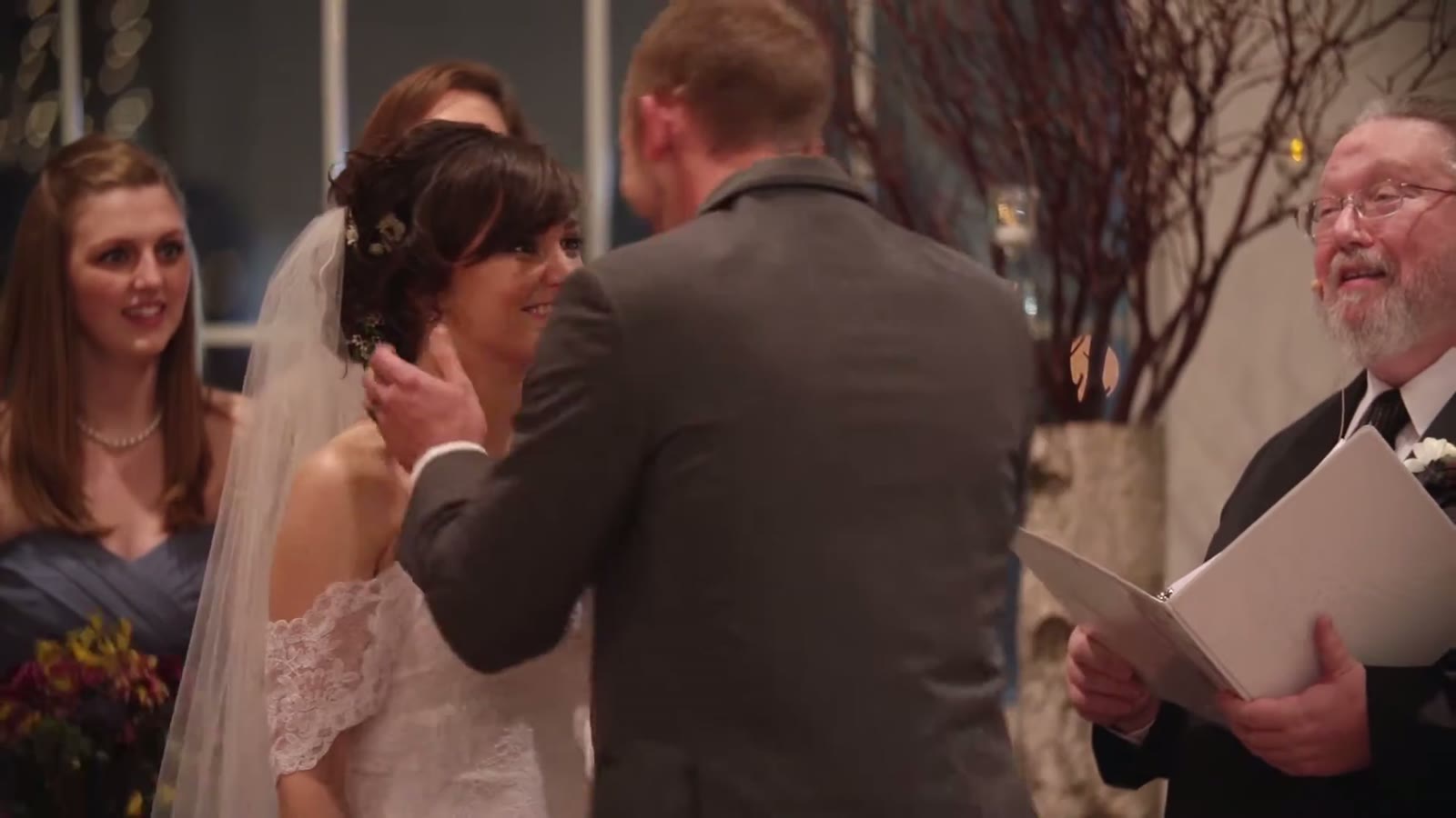 Groom wiping the bride's tear during the ceremony as the officiant reads from a book beside them