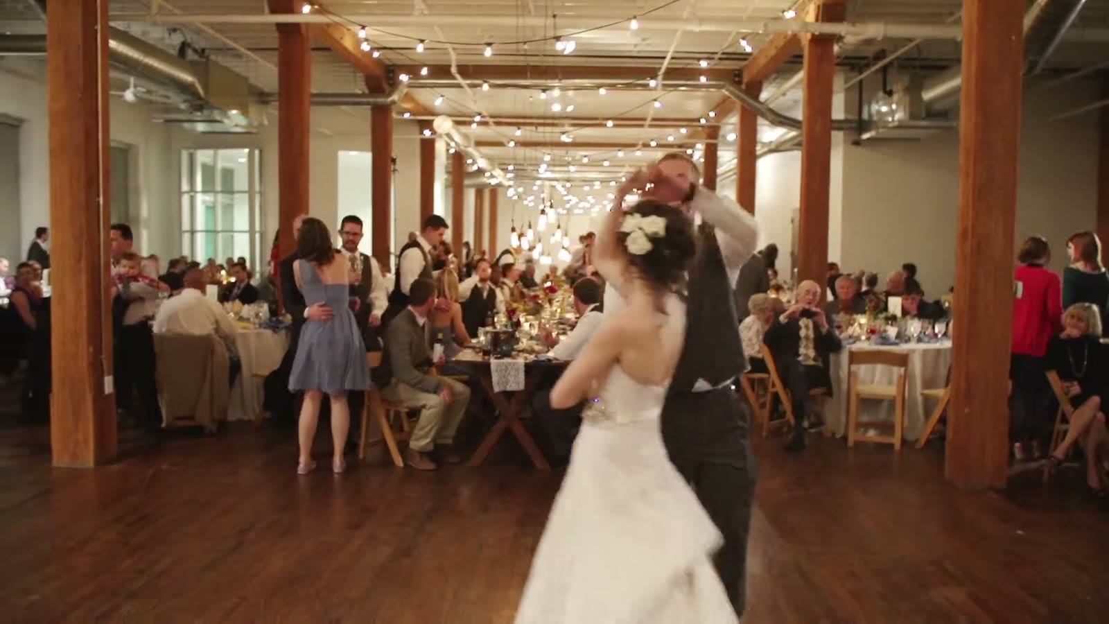 Bride and groom's first dance in a string-light-lined reception hall with guests seated at the tables