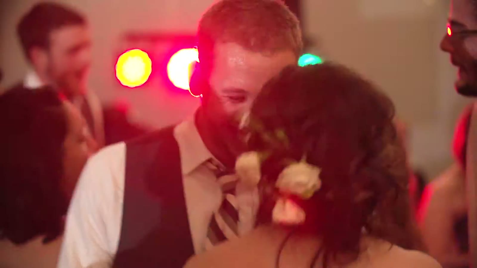 Close-up of the groom laughing with the bride on the dance floor, colored lights blurred behind them