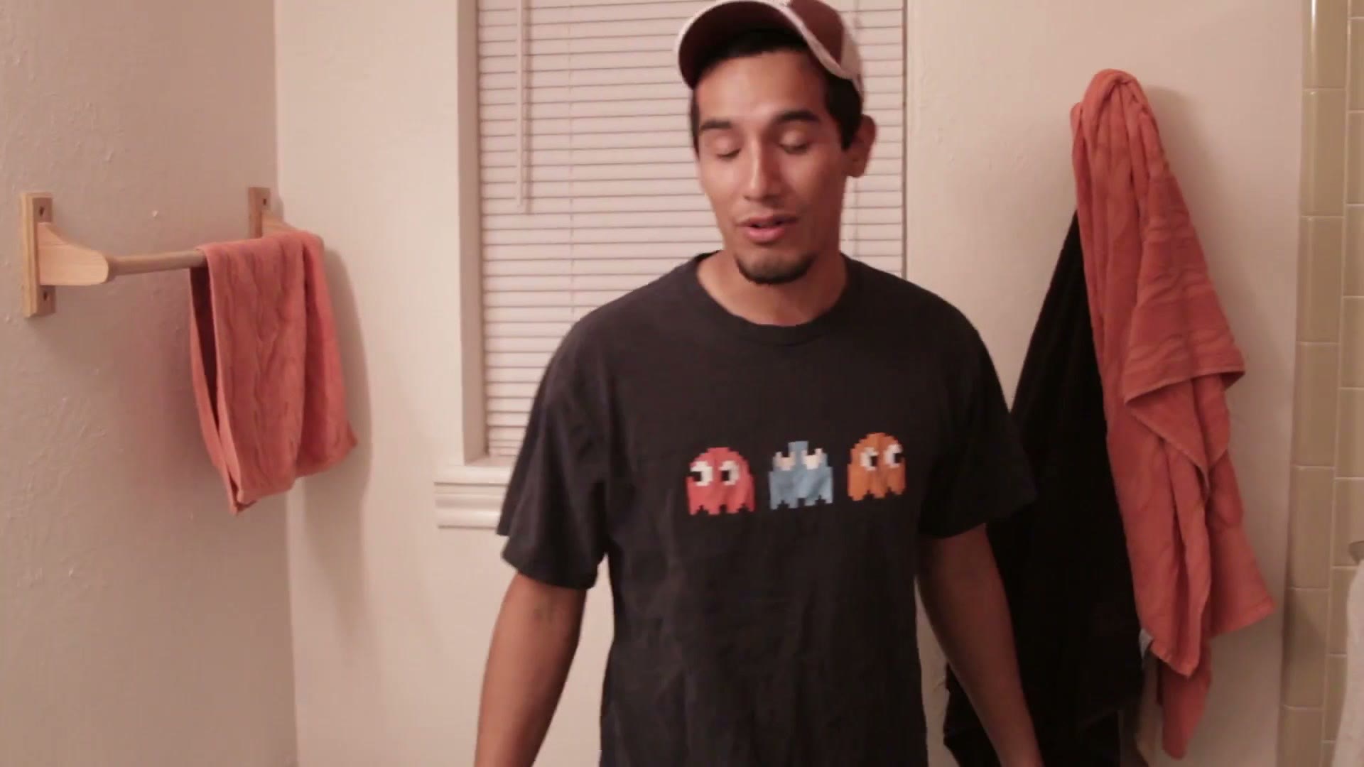 A young man standing in a small bathroom with towels on a rack behind him, explaining the final shot of the sequence to camera