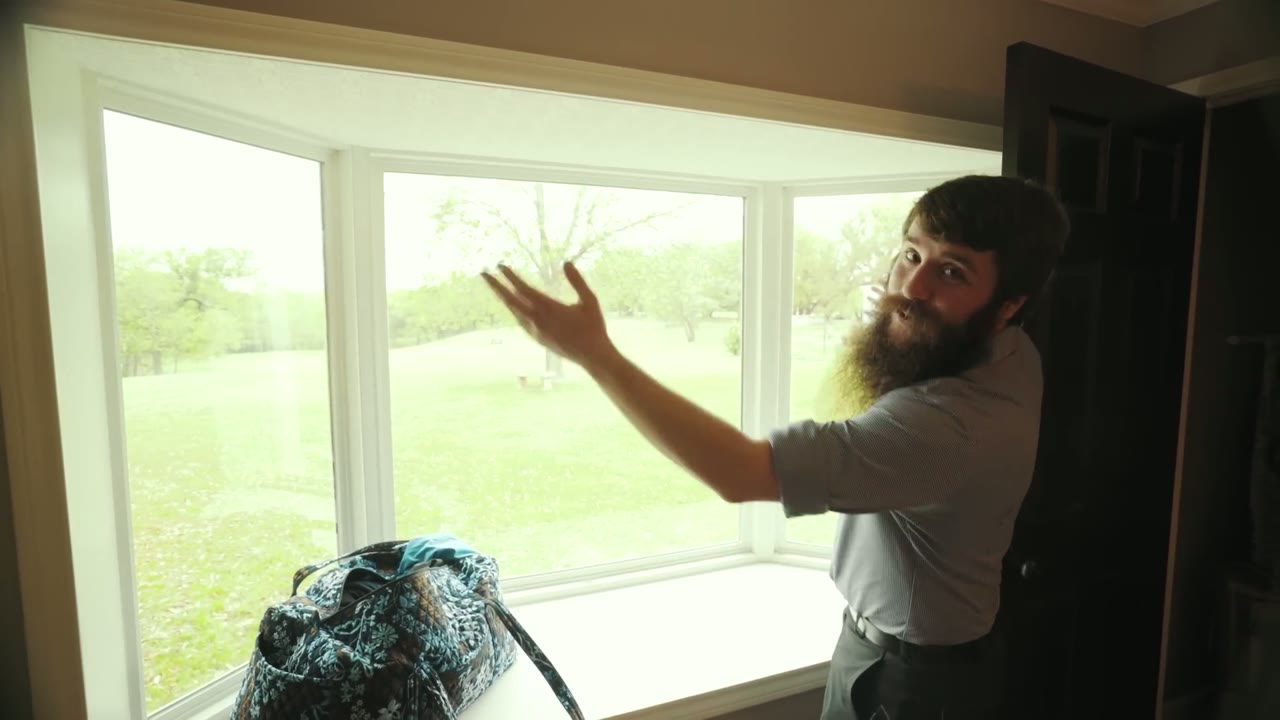 Matt gesturing toward a bay window with soft natural light, a floral bag sitting on the windowsill