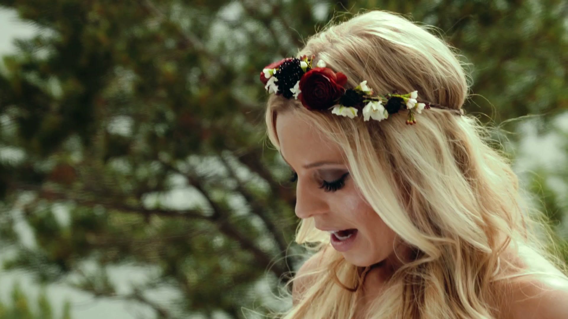 Close profile of the bride wearing a dark red and white flower crown against a blurred forest backdrop