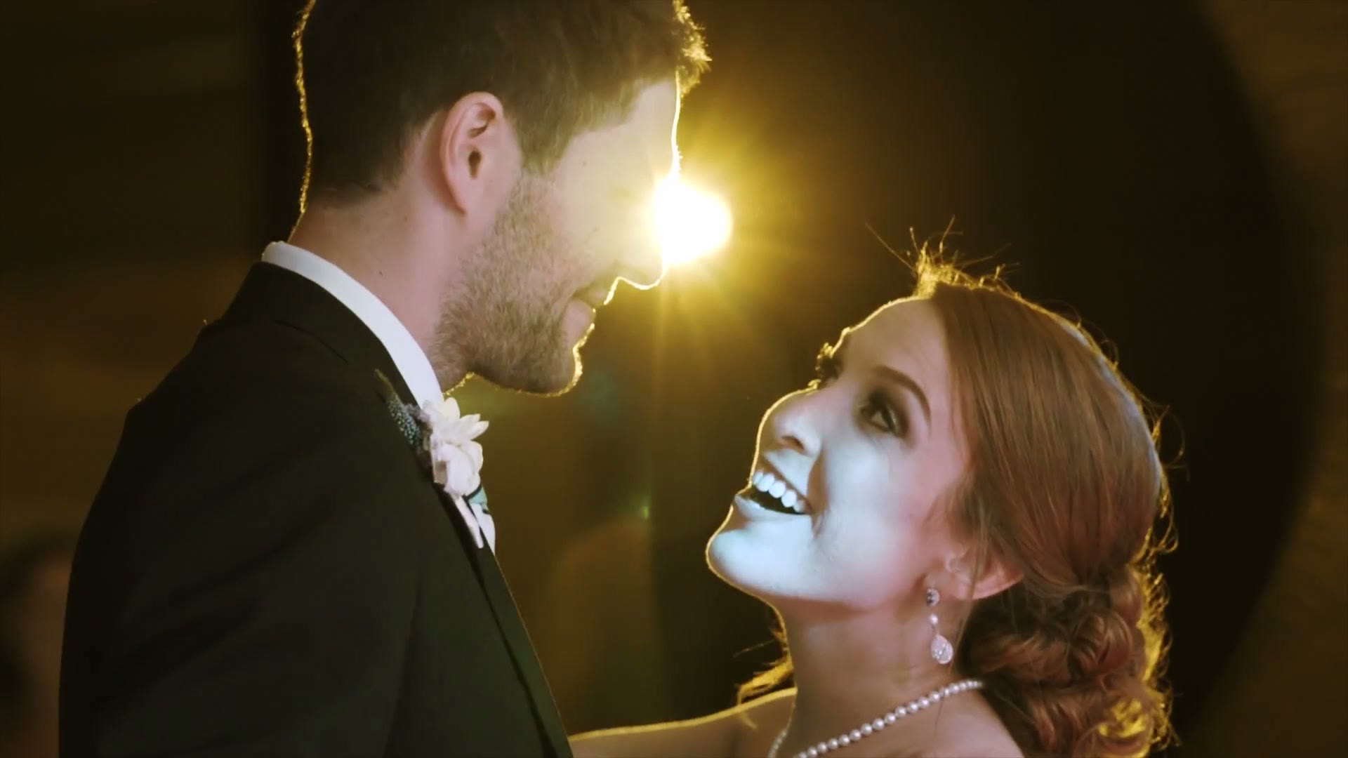 Bride and groom smiling and looking at each other close up, backlit by a warm light glowing between them