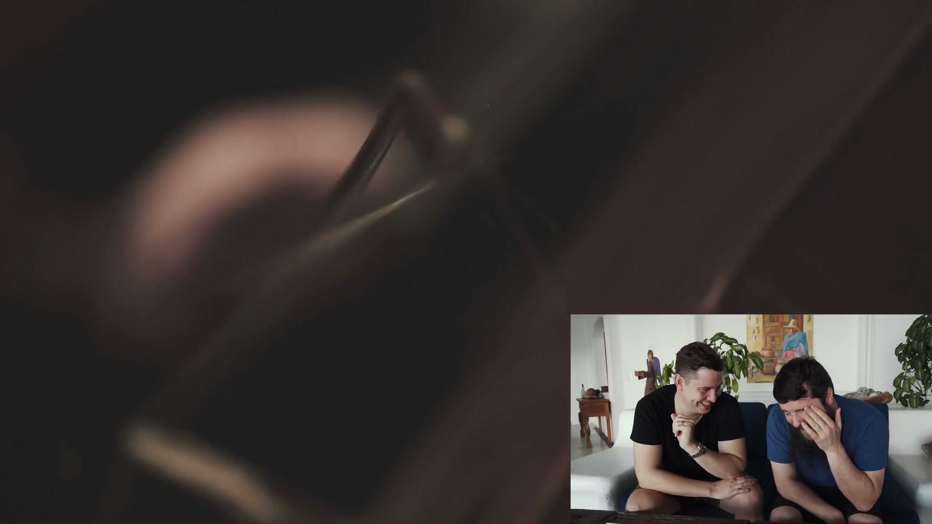 An almost entirely black frame with a faint out of focus shape in it, filmed at f/1.2, with Matt and Henry laughing in an inset.
