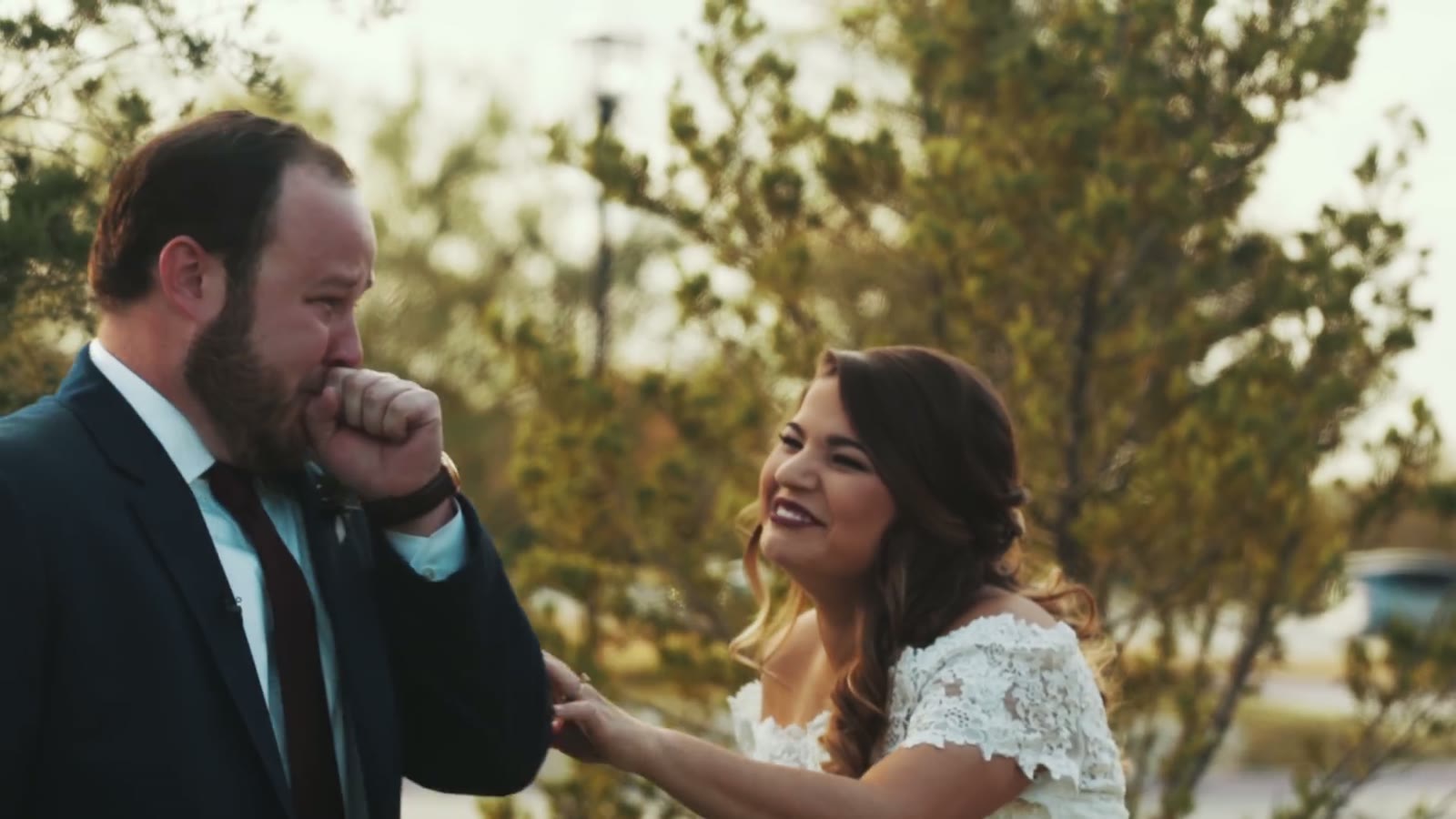 The groom wiping his eyes while the bride smiles at him outdoors