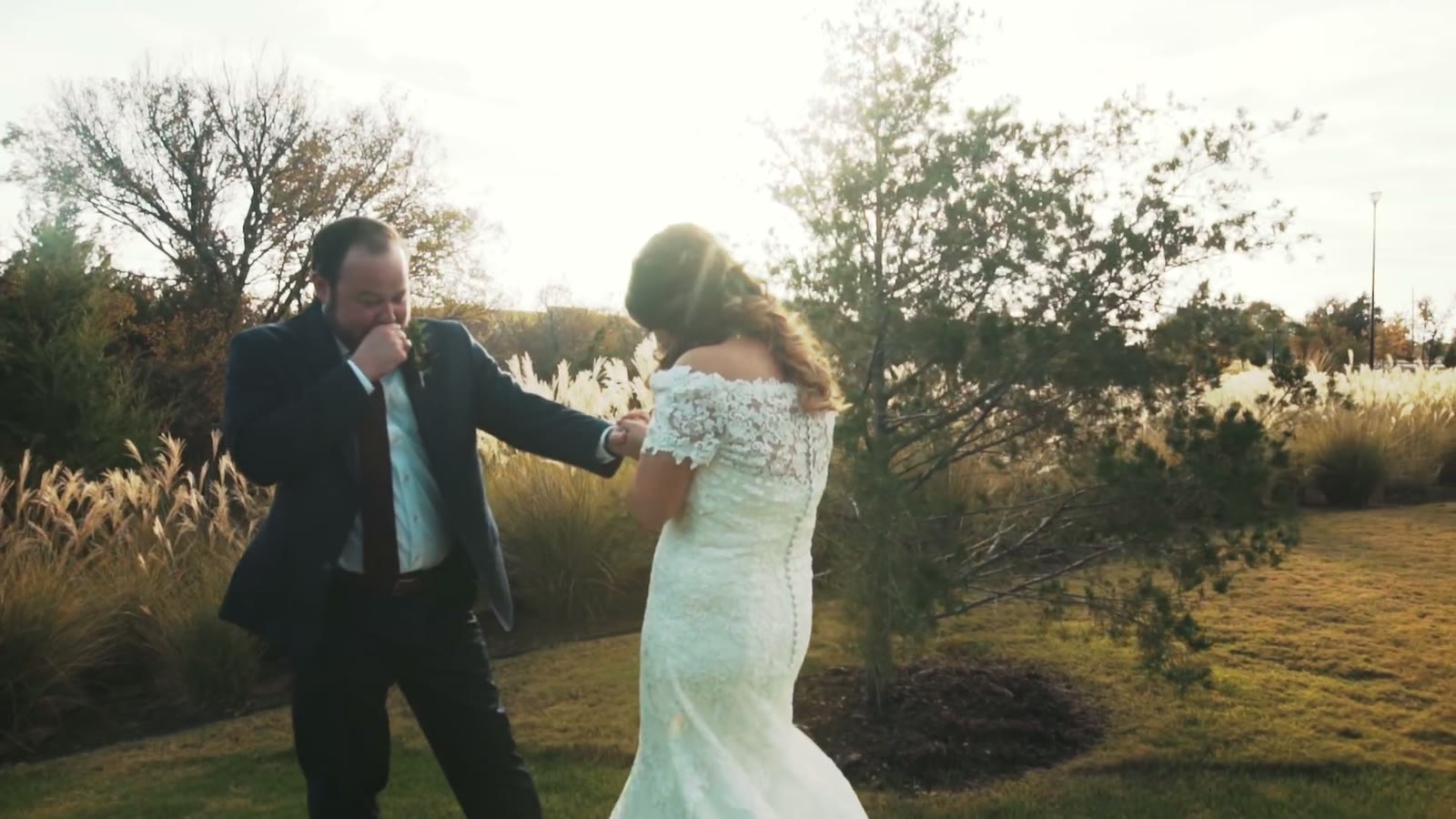 The couple walking hand in hand through a golden field at sunset