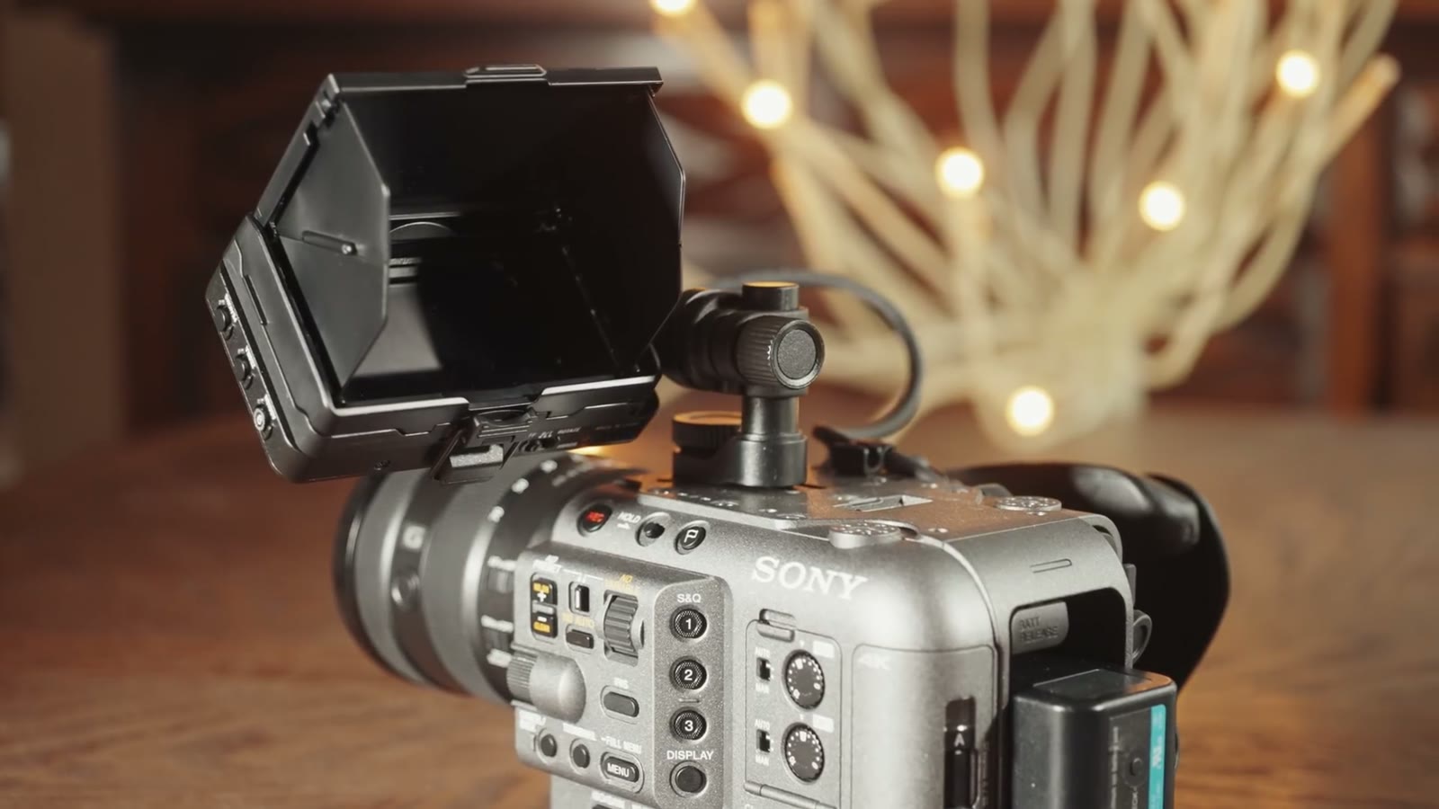 A Sony FX6 with the top handle attached and an external monitor mounted on it, sitting on a table in front of warm fairy lights