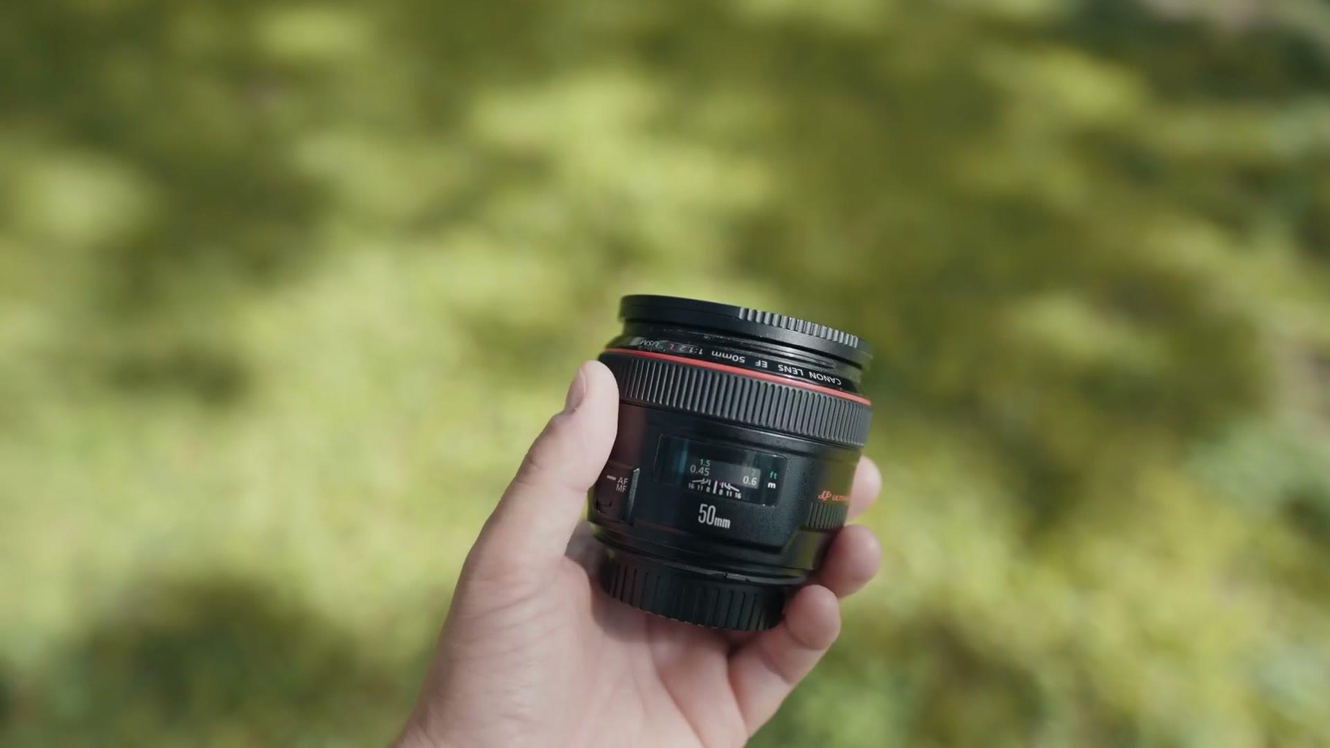 A Canon EF 50mm f/1.2 lens held up against blurred green foliage
