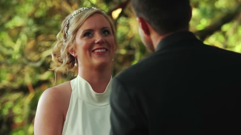 The bride smiling at the groom during the ceremony with the oak canopy of the family pasture out of focus behind them