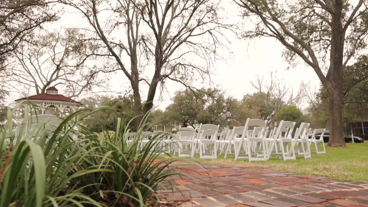 Rows of empty white folding ceremony chairs leading to a gazebo under a cloudy sky and bare trees
