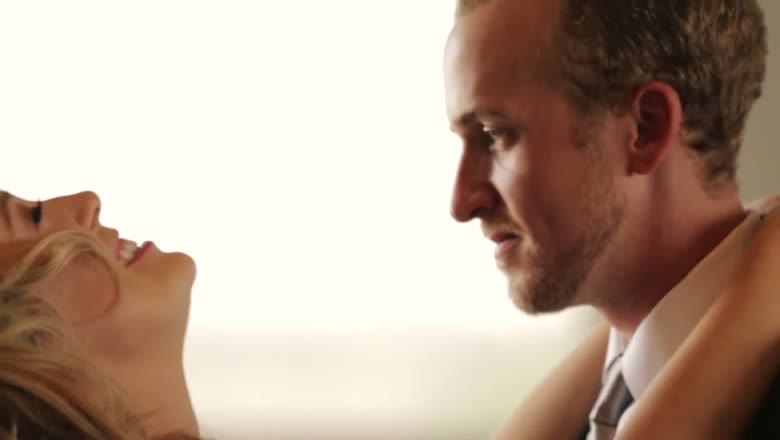 The bride laughing with her head tipped back while the groom looks at her in bright backlight