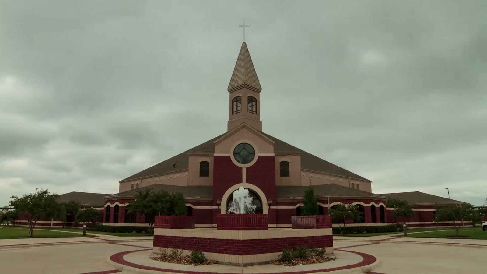Exterior of Christ United Methodist Church with its red brick facade, tall steeple, and fountain under an overcast sky