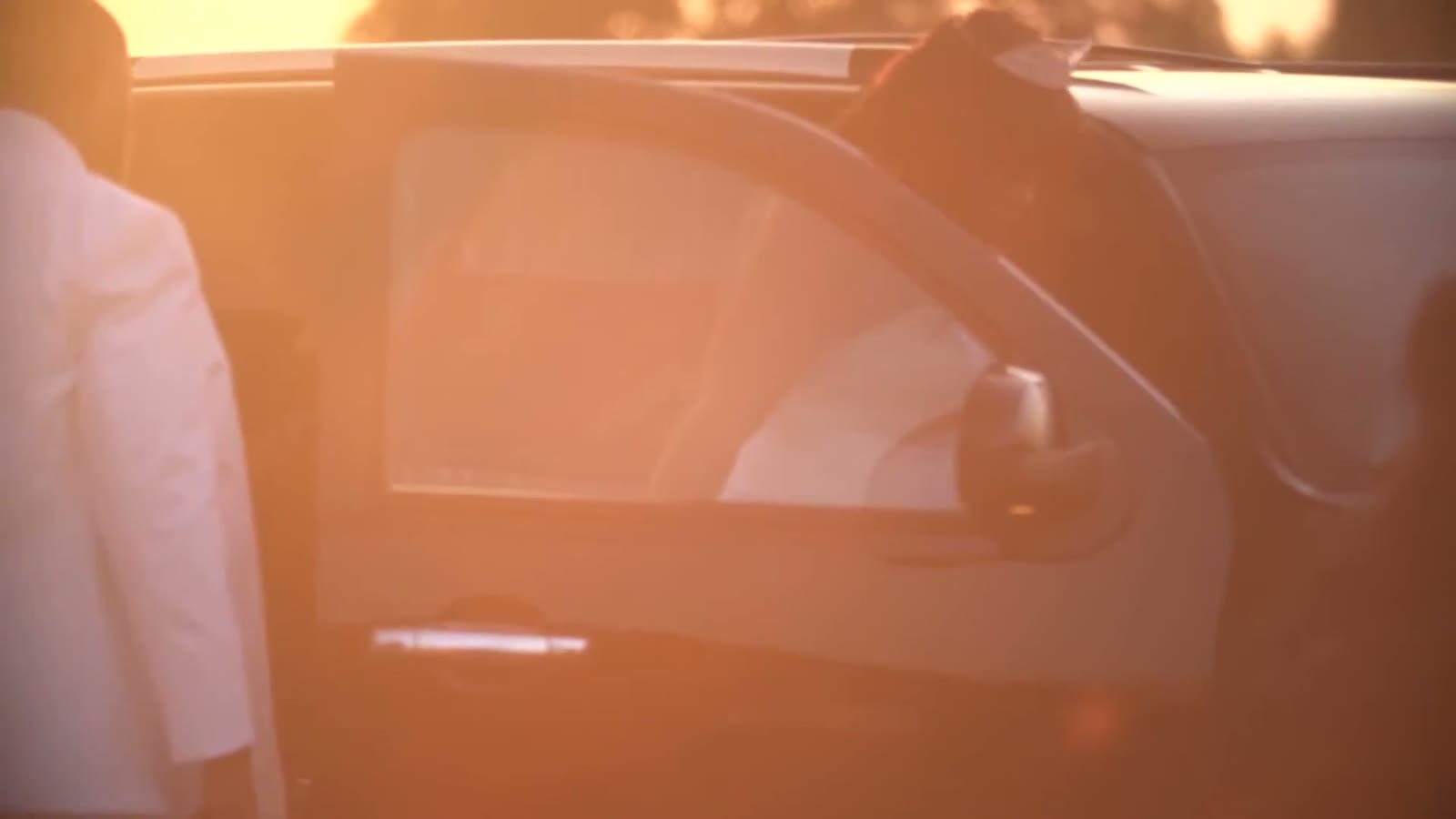 Backlit shot of someone getting into a car door at sunset with warm orange lens flare