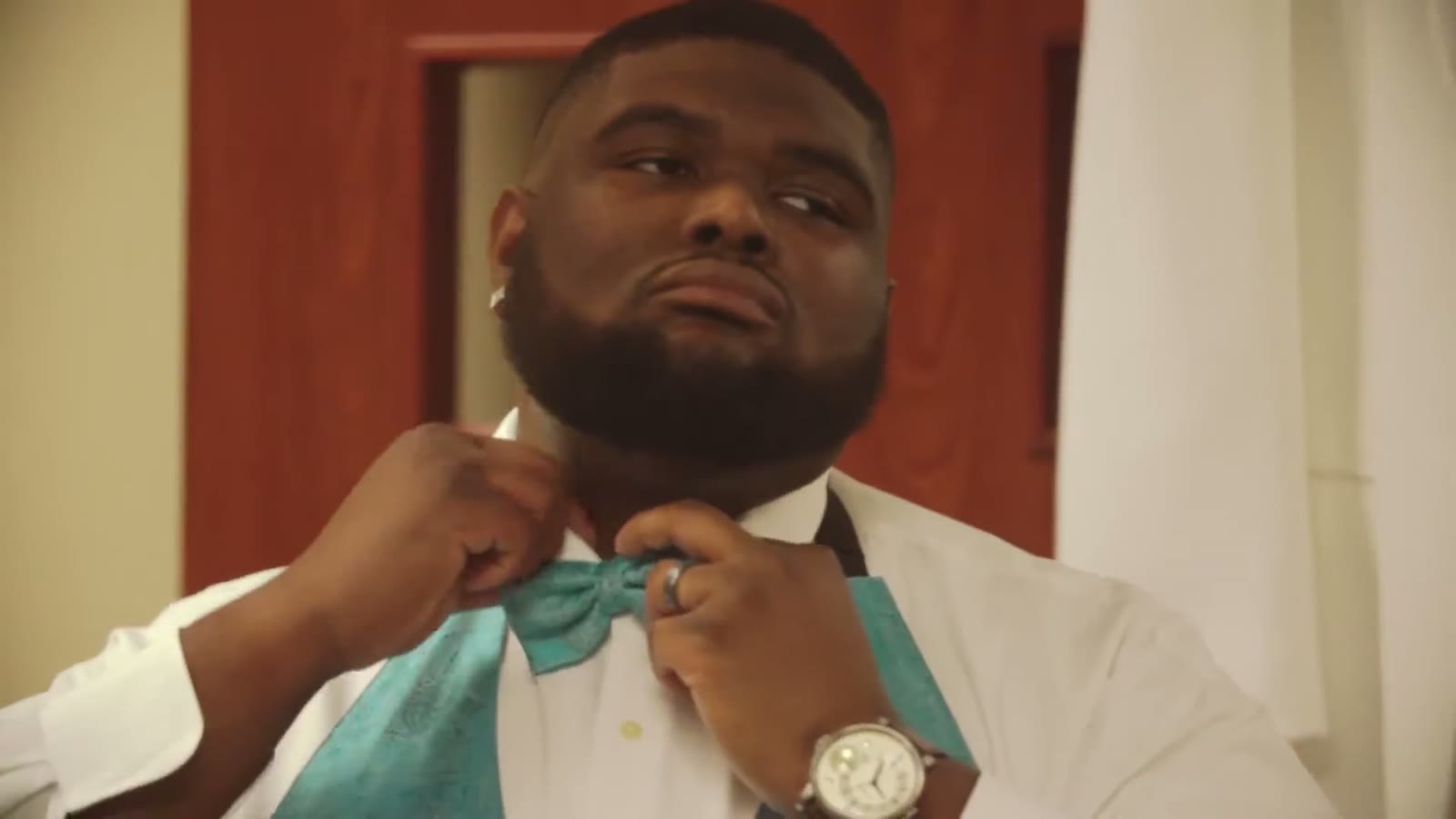 Close-up of the groom adjusting his teal bow tie in front of a mirror