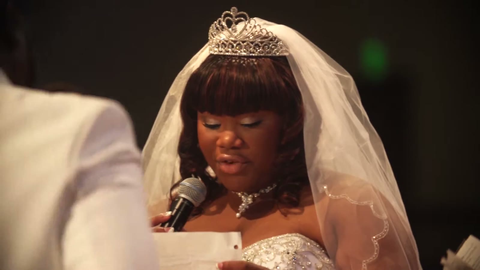 Bride in a tiara and veil speaking into a microphone while reading her vows
