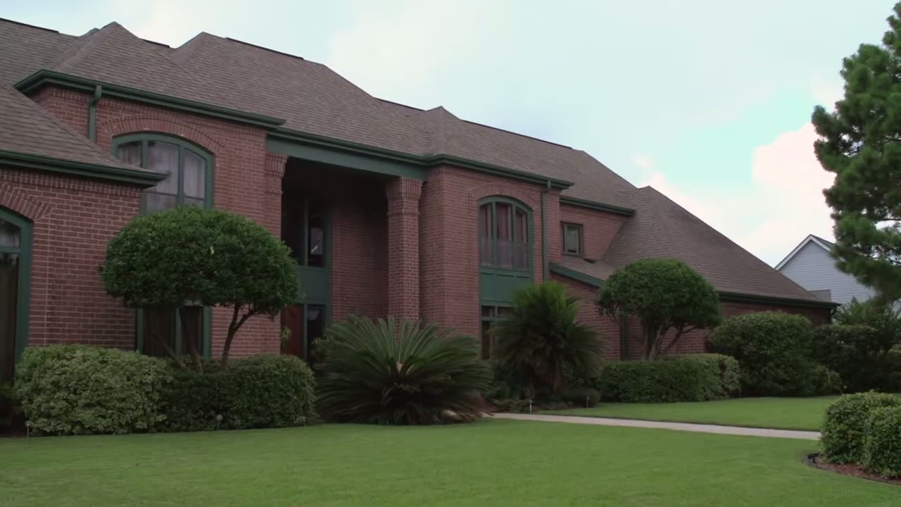 Exterior of a red brick building with green-trimmed windows and manicured hedges out front
