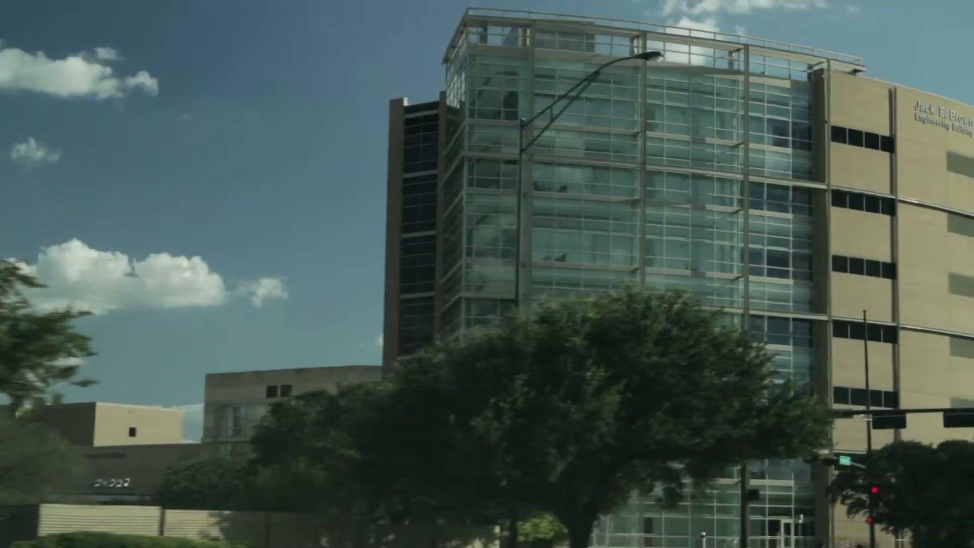 A large glass and stone university engineering building photographed from below against a blue sky with scattered clouds